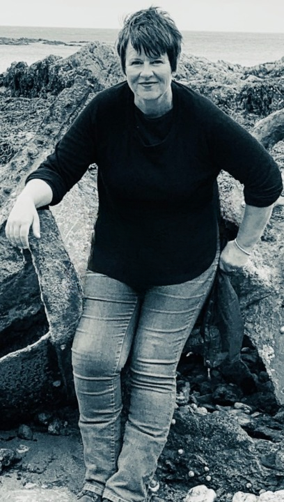 Nicky Osborne sitting by the sea in Cornwall, embodying calm, presence, and reflective wisdom