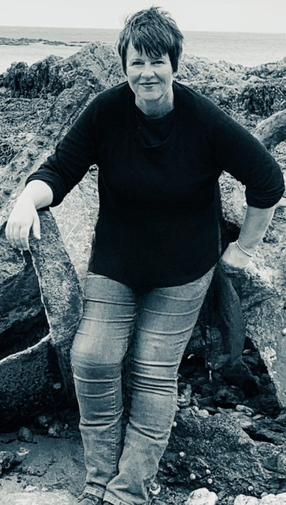 Nicky Osborne sitting by the sea in Cornwall, embodying calm, presence, and reflective wisdom