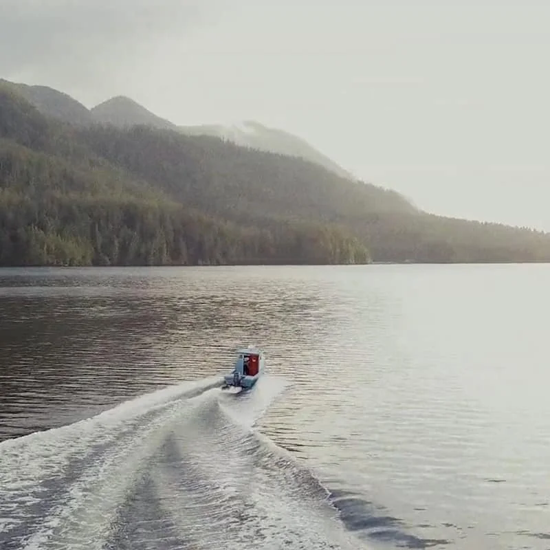 Un bateau naviguant sur un lac entouré de montagnes boisées, sous un ciel nuageux.