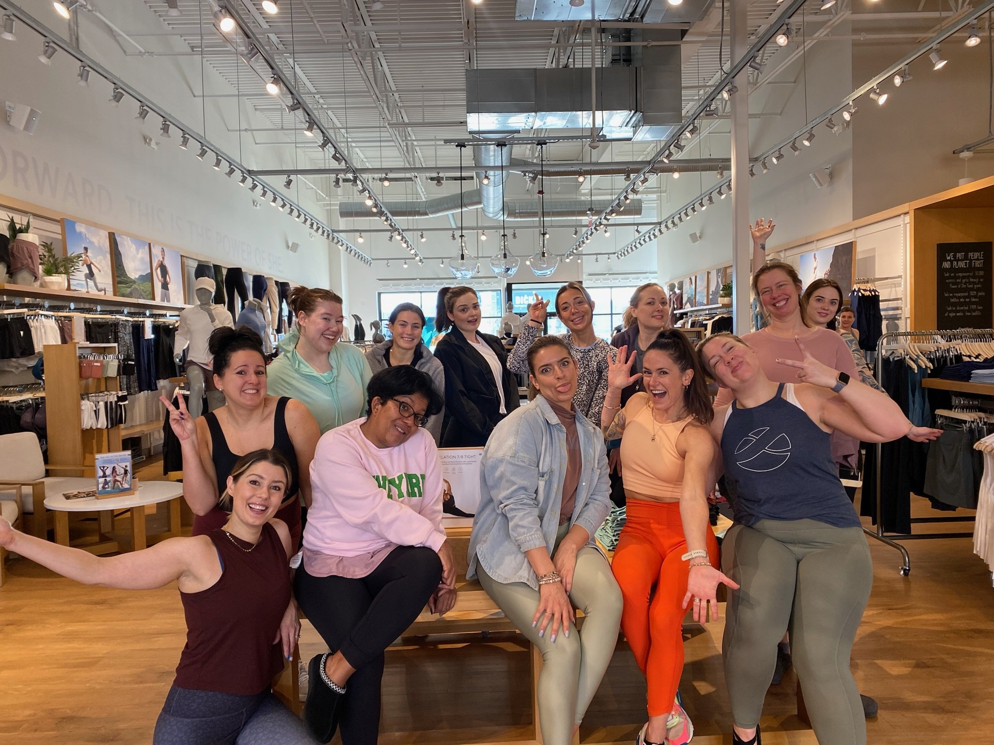 A group of women posing and smiling inside a clothing store, with mannequins and shelves of clothing in the background.