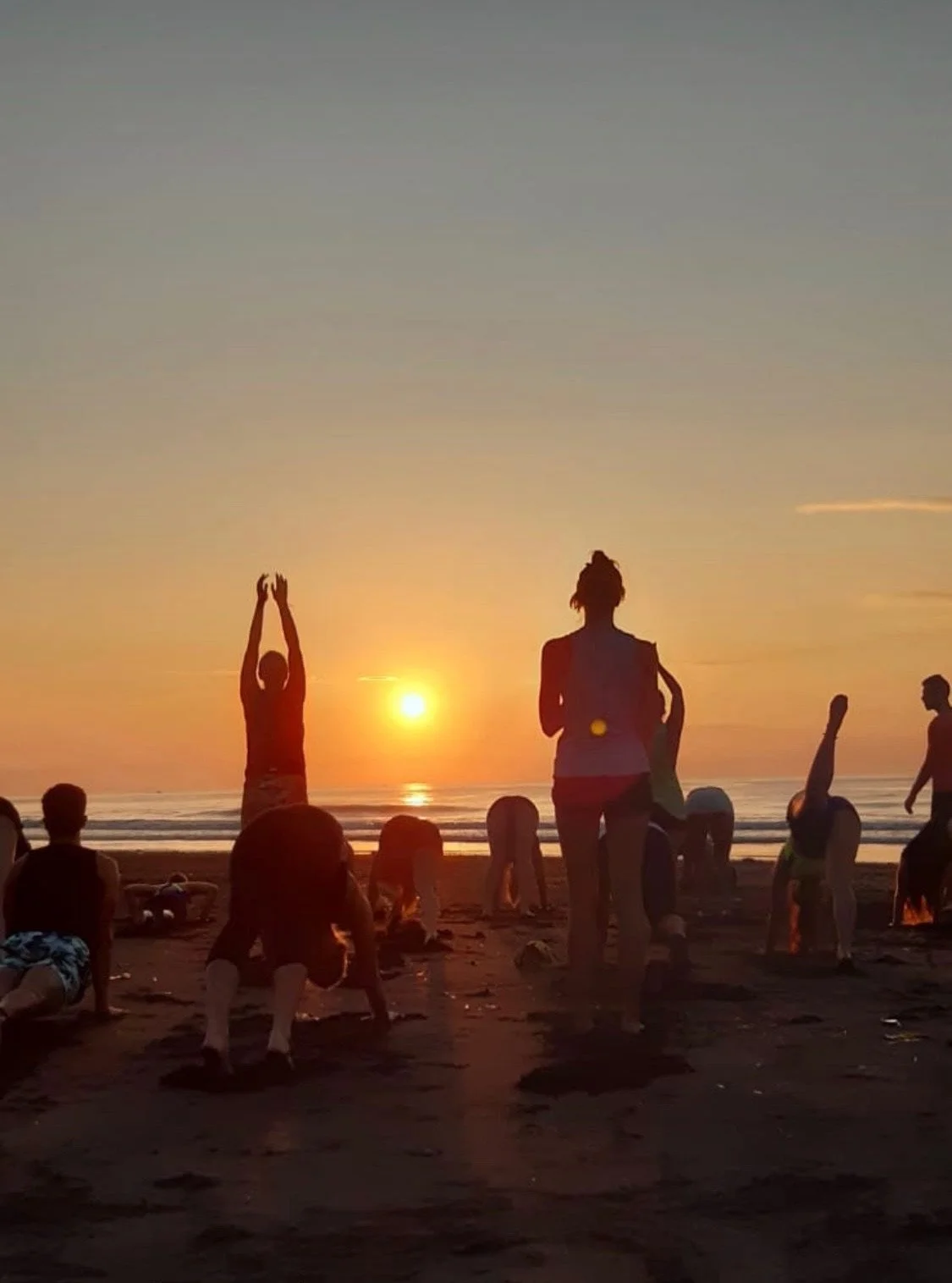 People practicing yoga on the beach at sunset.