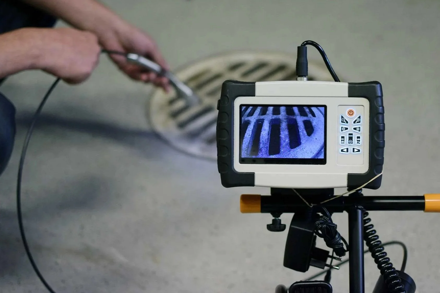 A person using a measuring device to inspect water flow in a drain.