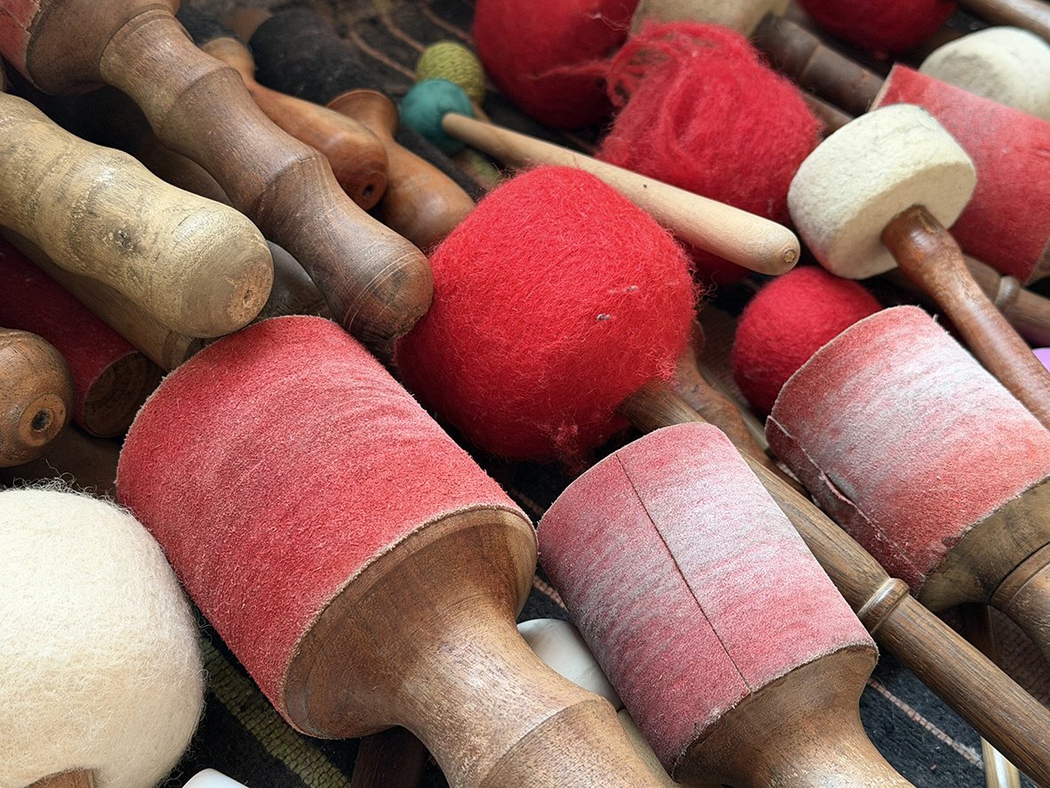 Verschiedene Holzstampfer, einige mit roten und weißen Filzauflagen, liegen auf einem Tisch.