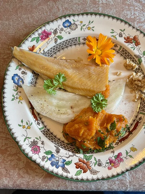 Ein Teller mit Fisch, Gemüse und einer essbaren Blume, serviert auf einem dekorativen Porzellanteller.