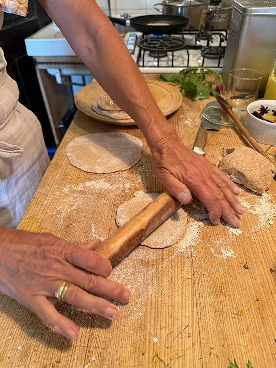 Person rollt Teig mit einem Holzroller auf einer Holzarbeitsfläche aus.