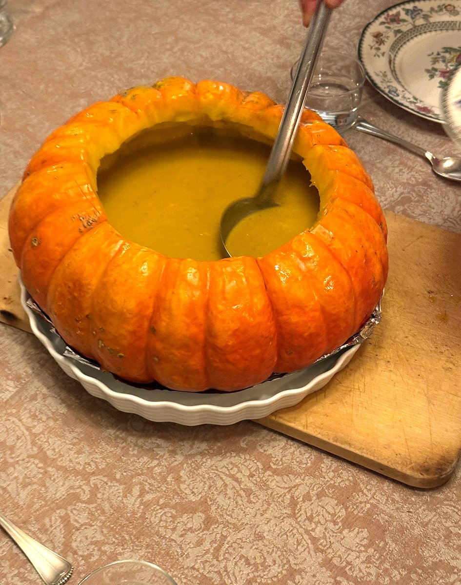 Kürbissuppe in einem ausgehöhlten Kürbis auf einem Tisch mit Tellern und Besteck