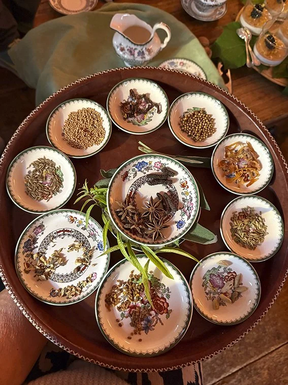 Verschiedene Gewürze und Kräuter in kleinen Schälchen auf einem runden Tablett, darunter Zimtstangen, Anissamen, und getrocknete Kräuter.