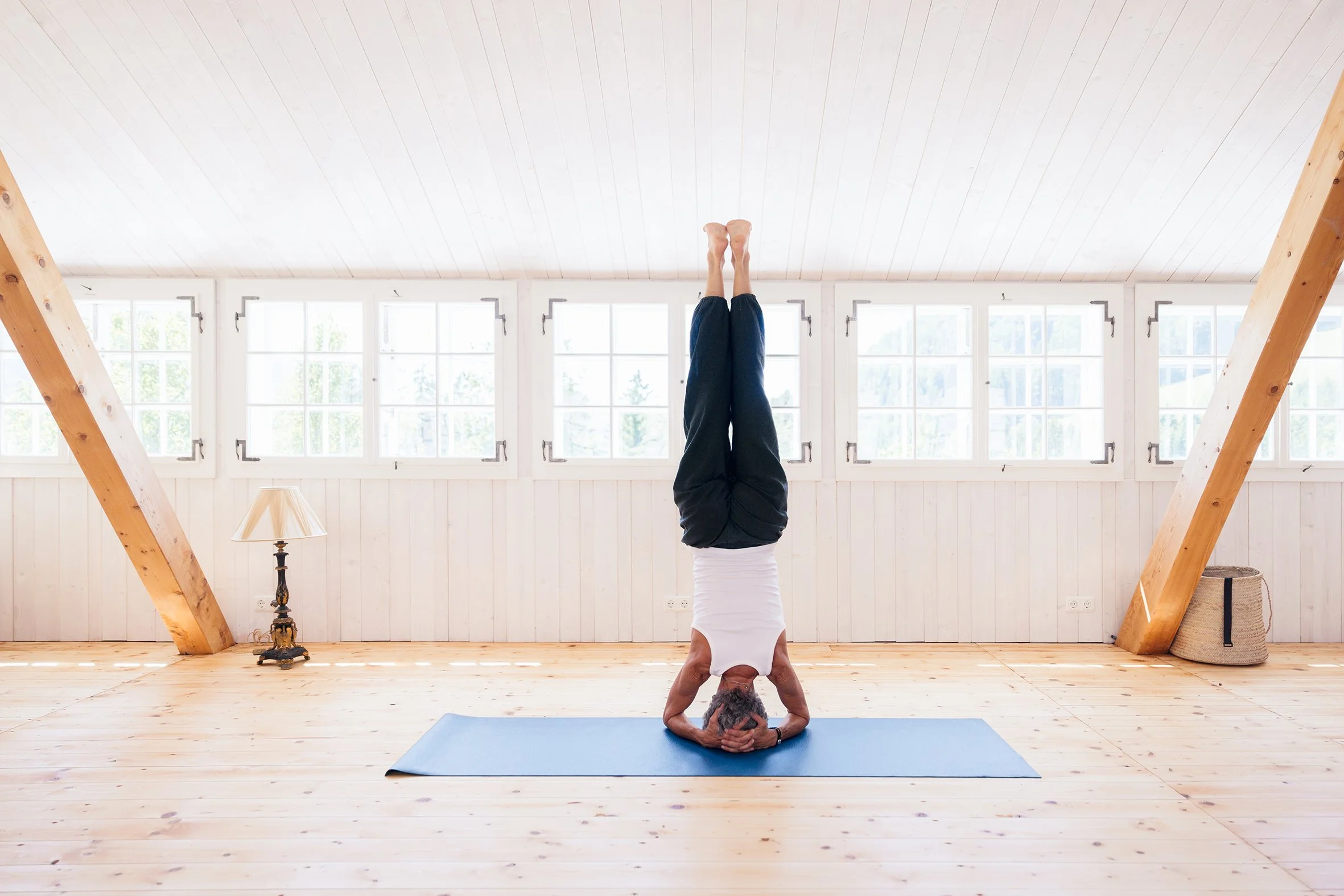 Frau übt den Kopfstand auf Yoga-Matte in hellem Raum mit großen Fenstern
