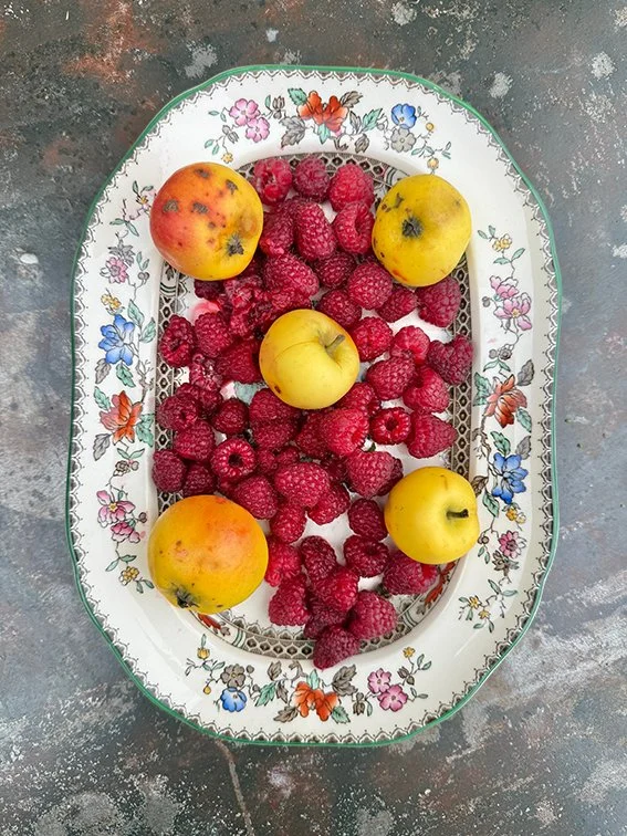 Buntes Obst, bestehend aus vier Äpfeln und einer Vielzahl von Himbeeren, auf einem dekorativen ovalen Tablett