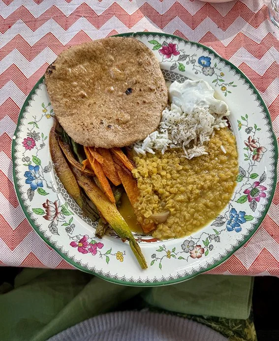 Traditioneller indischer Thali mit flatbread, gelbe Linsensuppe, weißem Joghurt, gekochtem Gemüse und Reis, serviert auf einer festlichen Blumen-Teller mit rotem und weißem Muster.