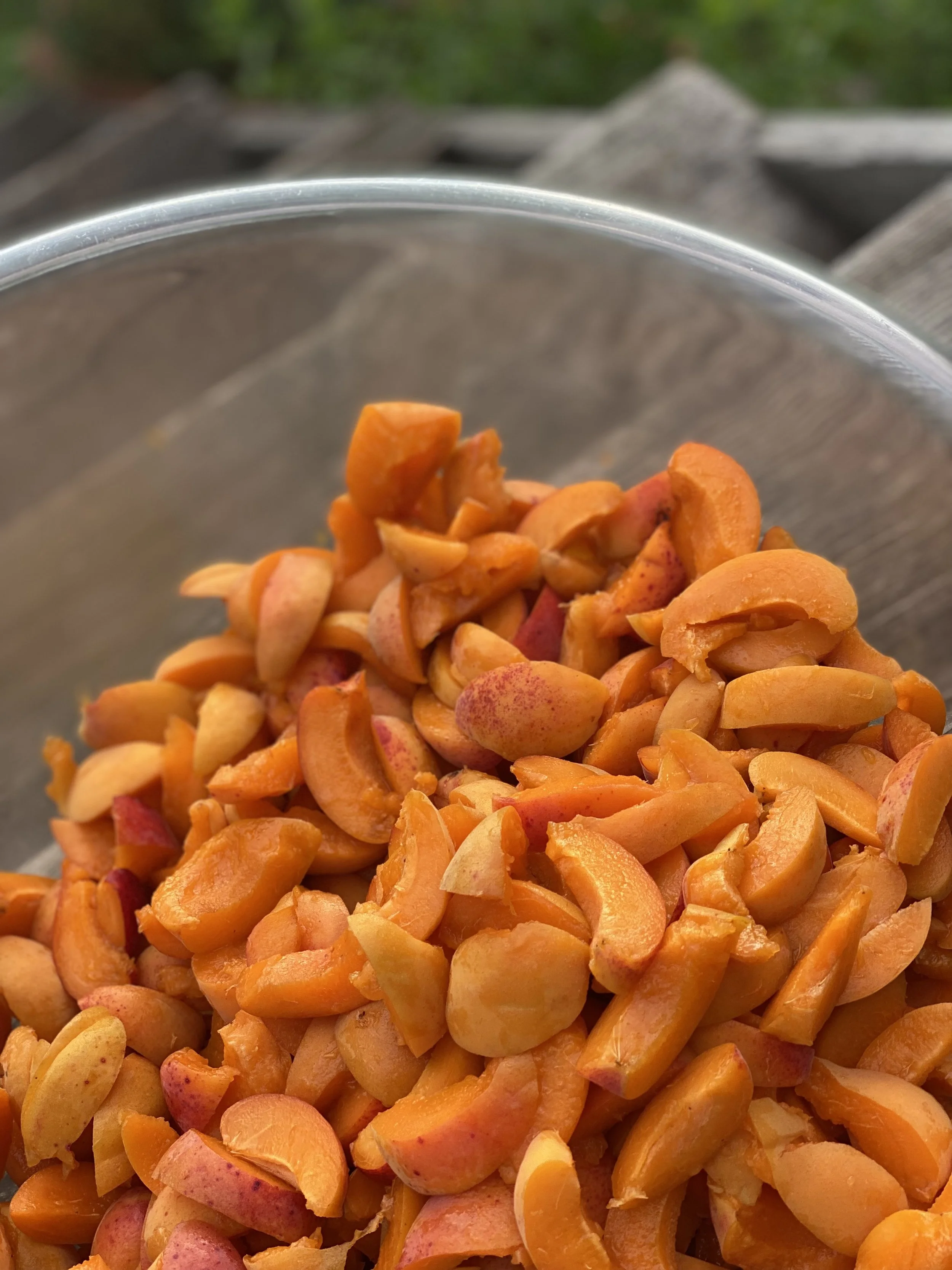 Ein Glas mit gewaschener und geschnittener Aprikose, vor einem holzfarbenen Hintergrund im Freien.