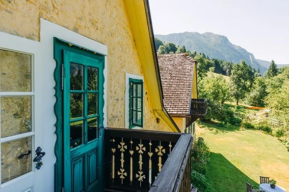 Blick von einem Balkon auf eine grüne Landschaft mit Bäumen und Bergen im Hintergrund.