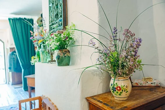 Blumenarrangements in farblich verzierten Keramikvasen auf einer weißen Kommode und einem Holzschrank in einem rustikalen Raum.
