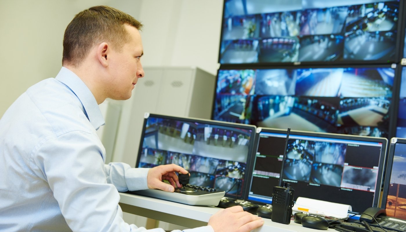 Security control room operator monitoring multiple screens displaying surveillance footage.