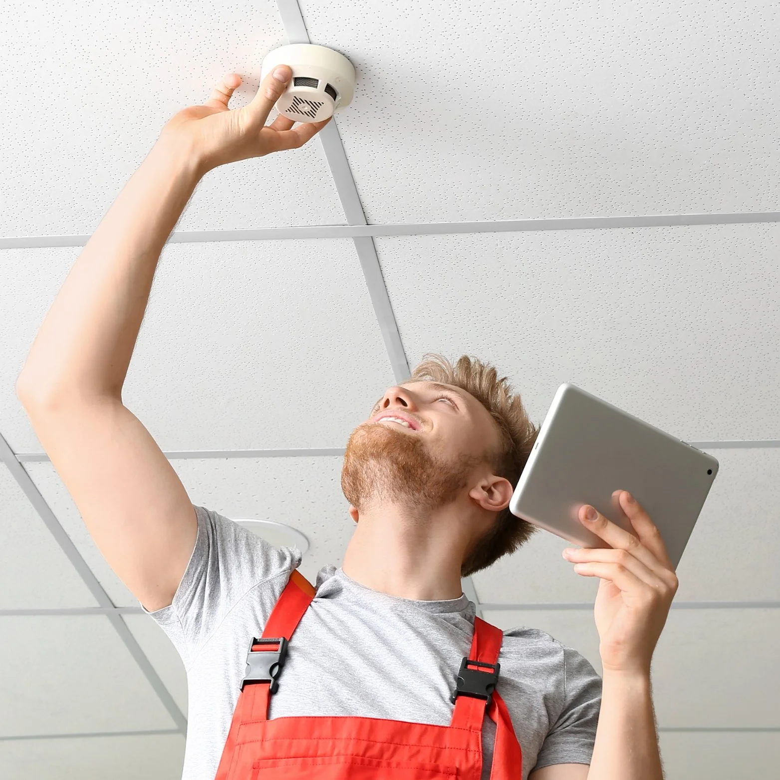 A man installing a smoke detector on the ceiling in an office building.