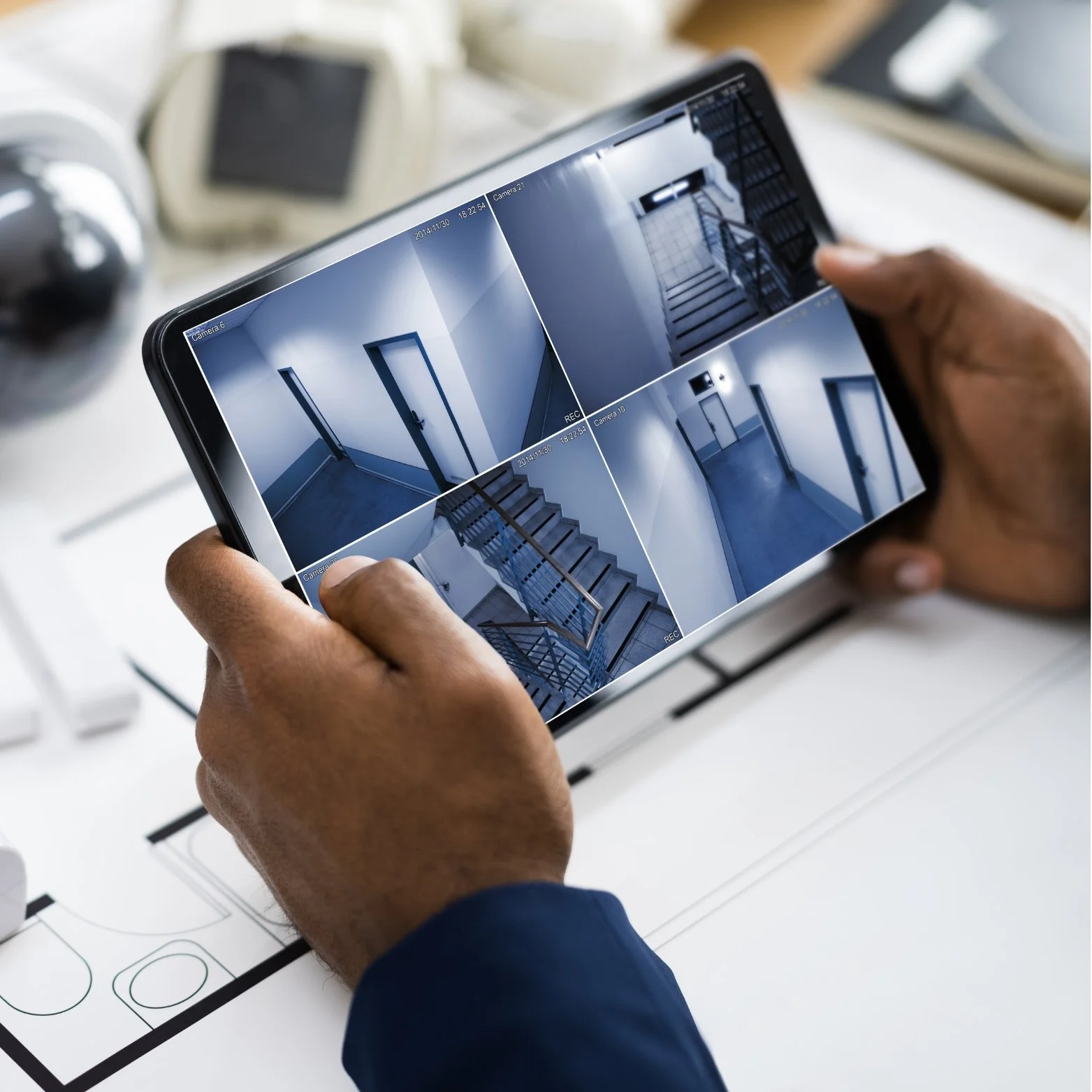 Person holding a tablet monitoring security camera feeds of a staircase and hallway.
