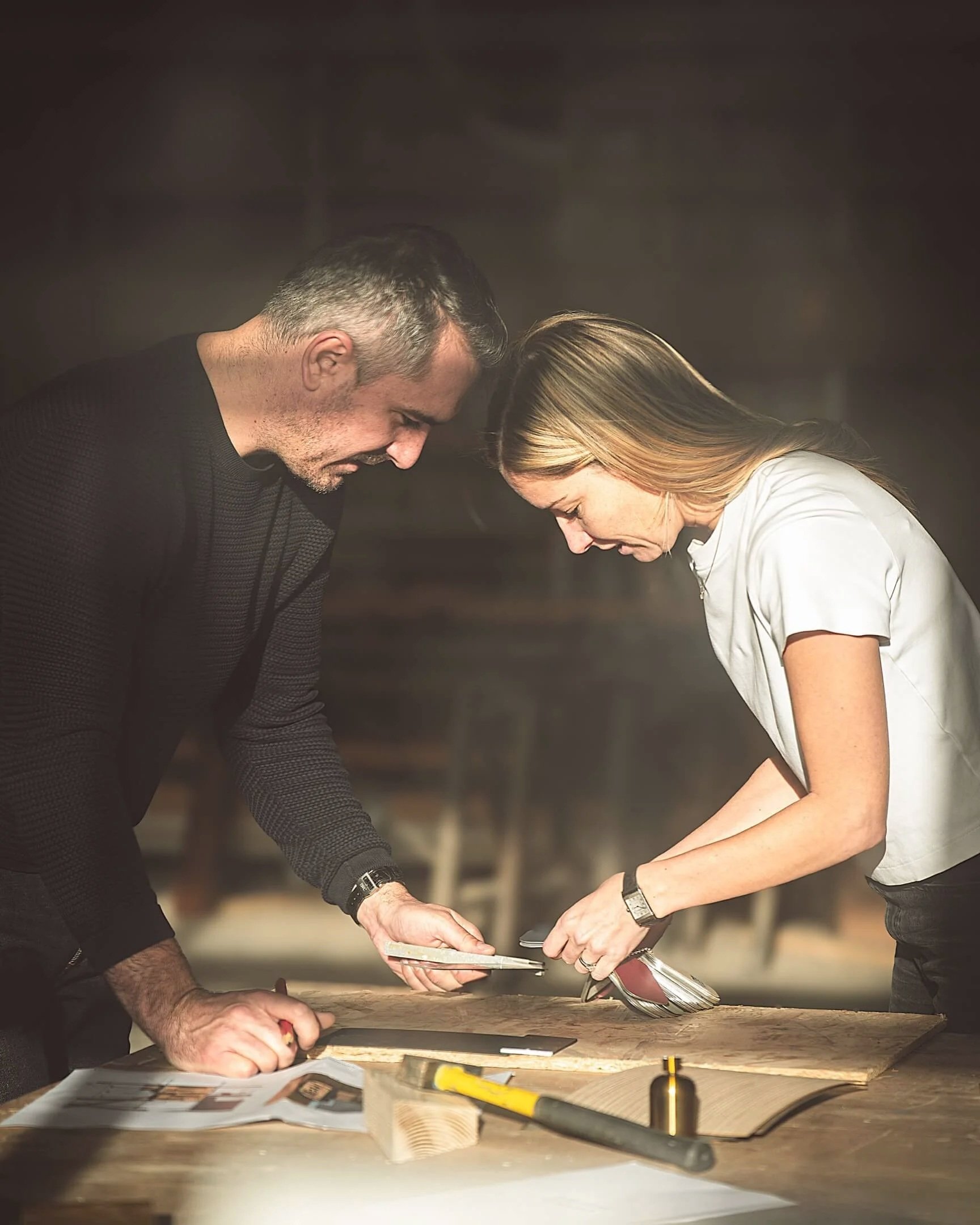 Anne et Jeremy, fondateurs d'Anjem Studio face à face, inclinées vers une table, travaillant sur un projet, dans leur atelier aux Rousses