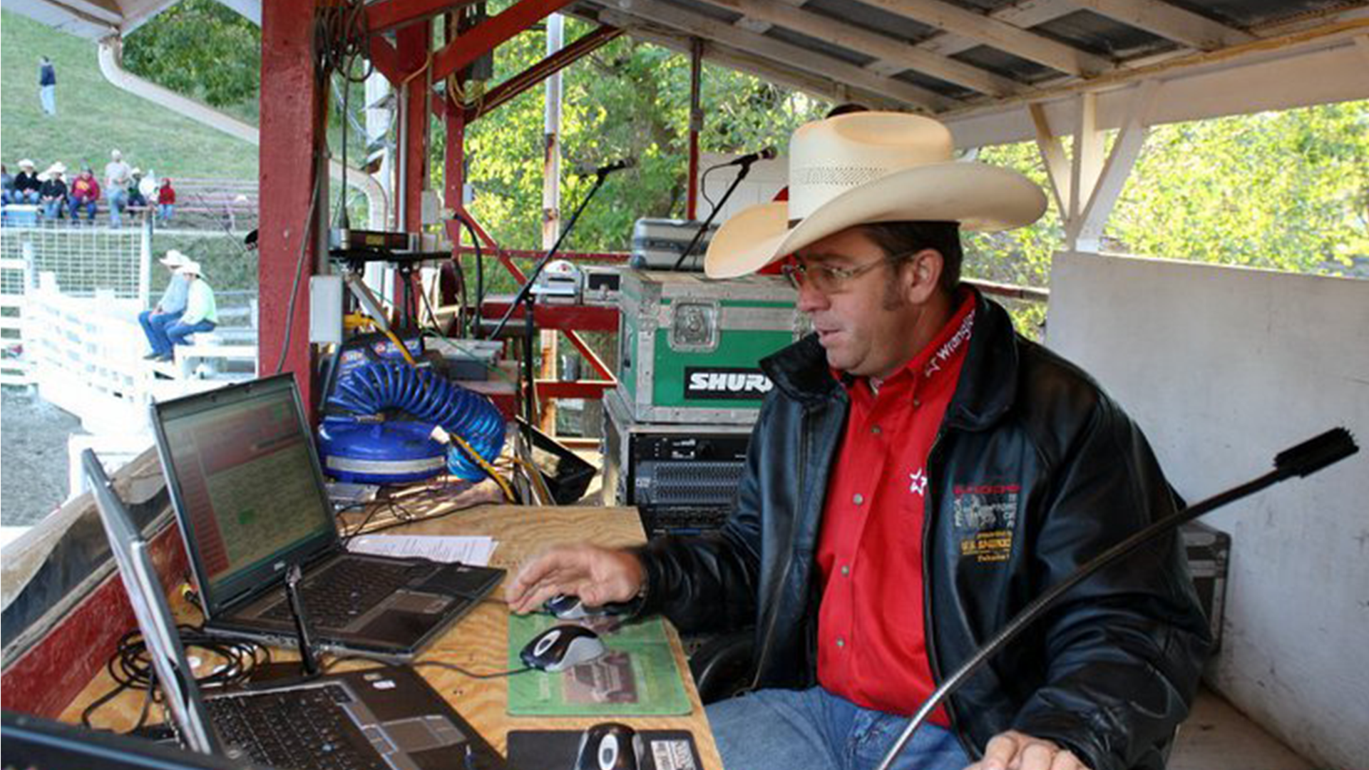 Man wearing cowboy hat and red shirt operating laptop at rodeo event