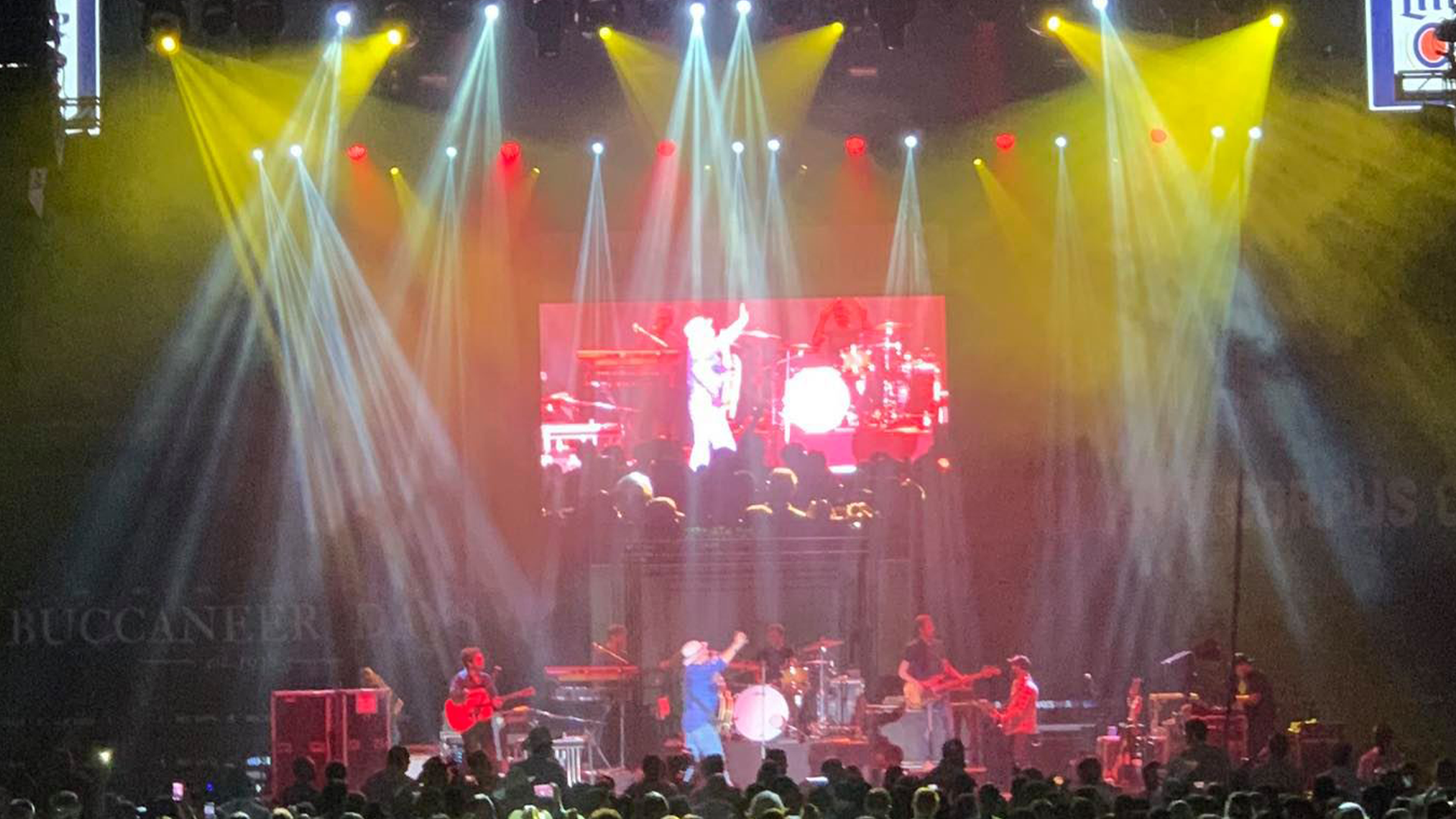 Live concert stage with band performing, colorful lighting, and an audience watching.