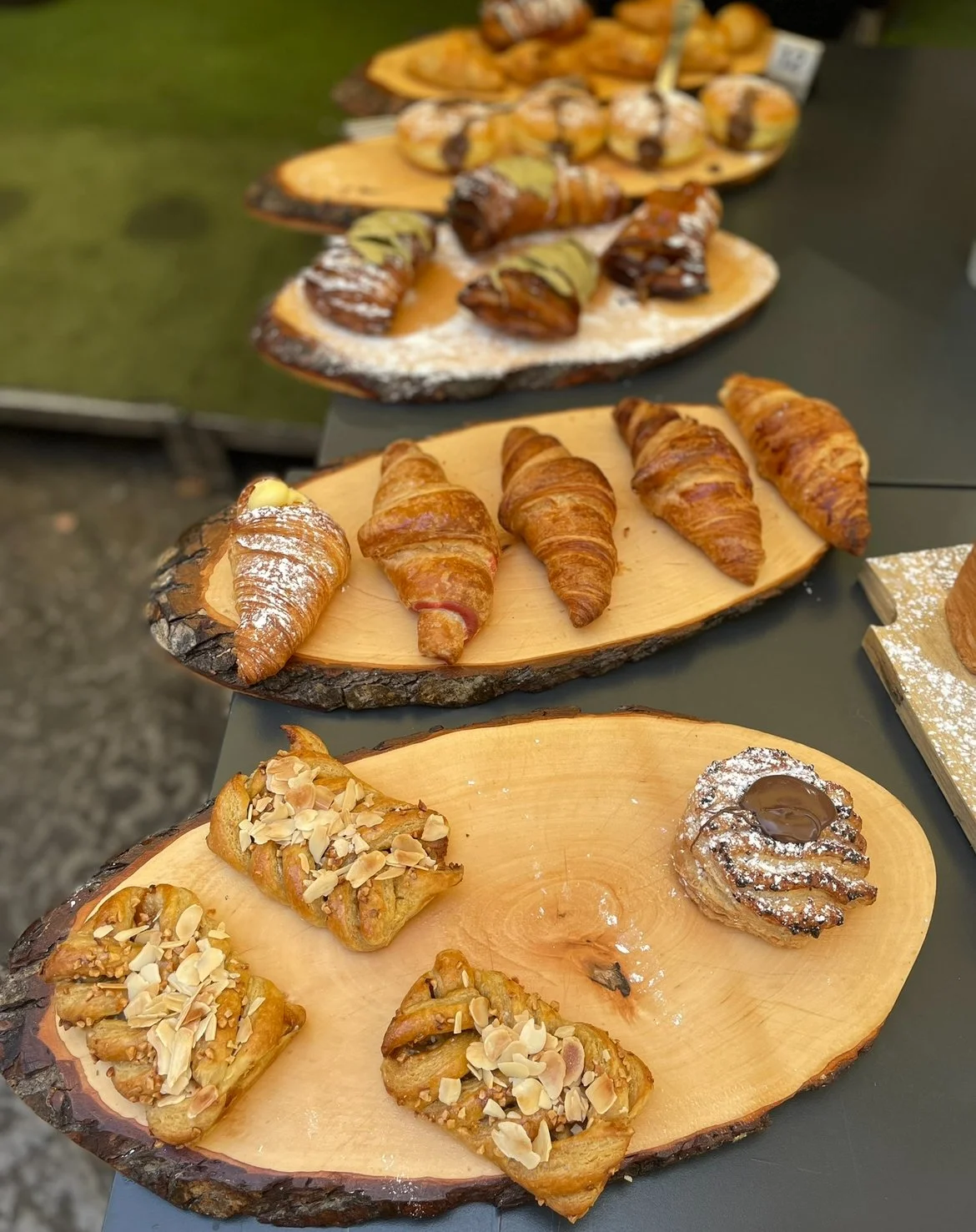 Assorted pastries including croissants, almond danishes, and chocolate-filled pastries arranged on wooden slabs.