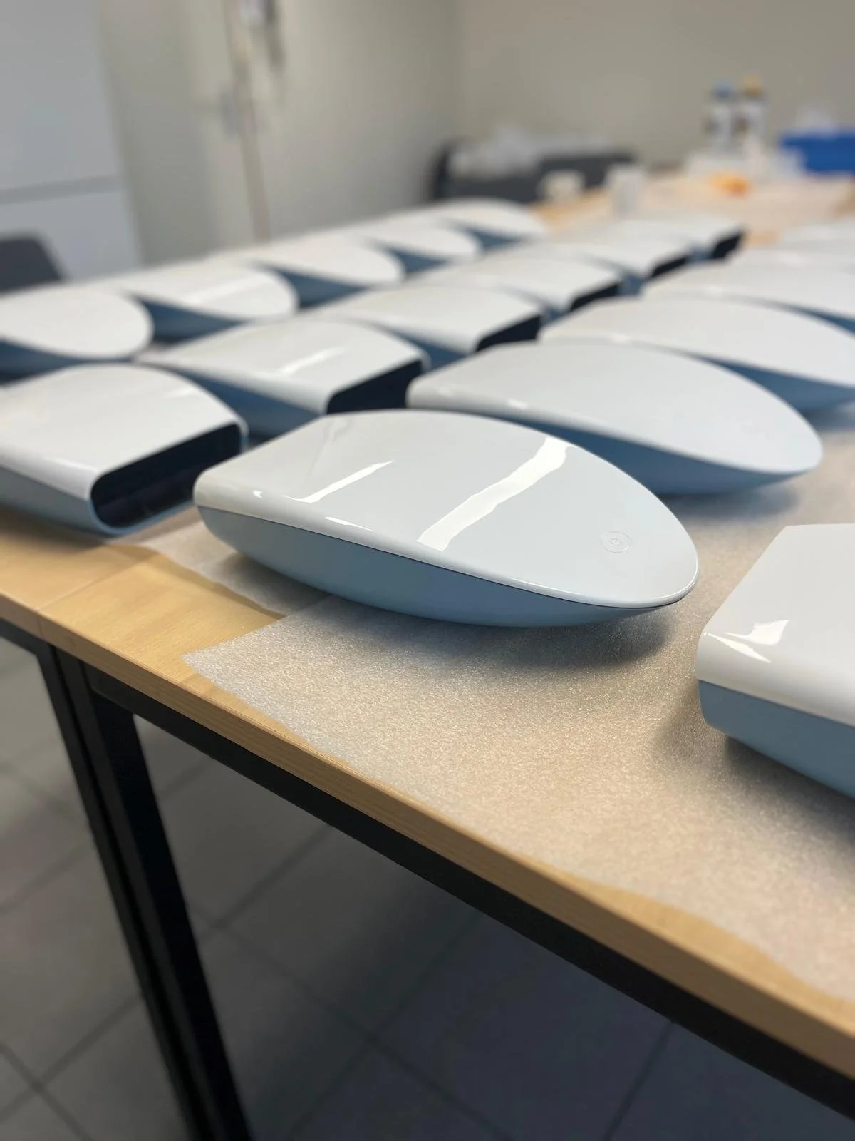 Multiple white, glossy, teardrop-shaped objects arranged in rows on a wooden table.