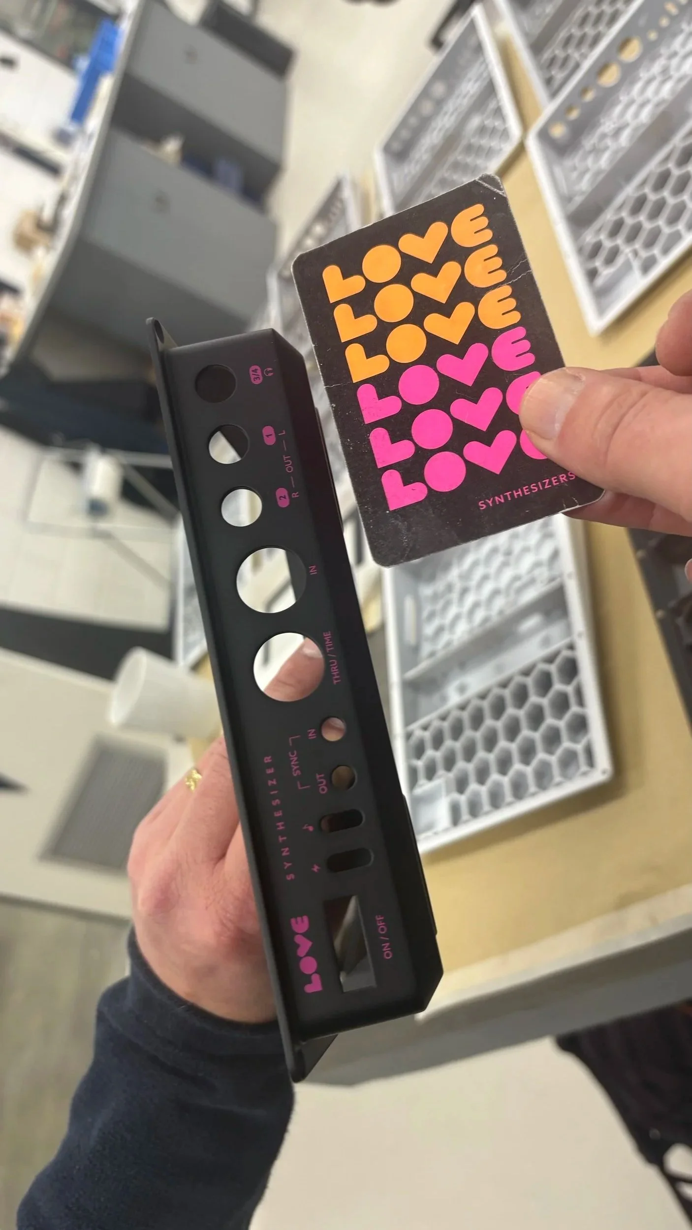 A person holds a vintage synthesizer module and a sticker sheet with the word "LOVE" in orange and pink colors.