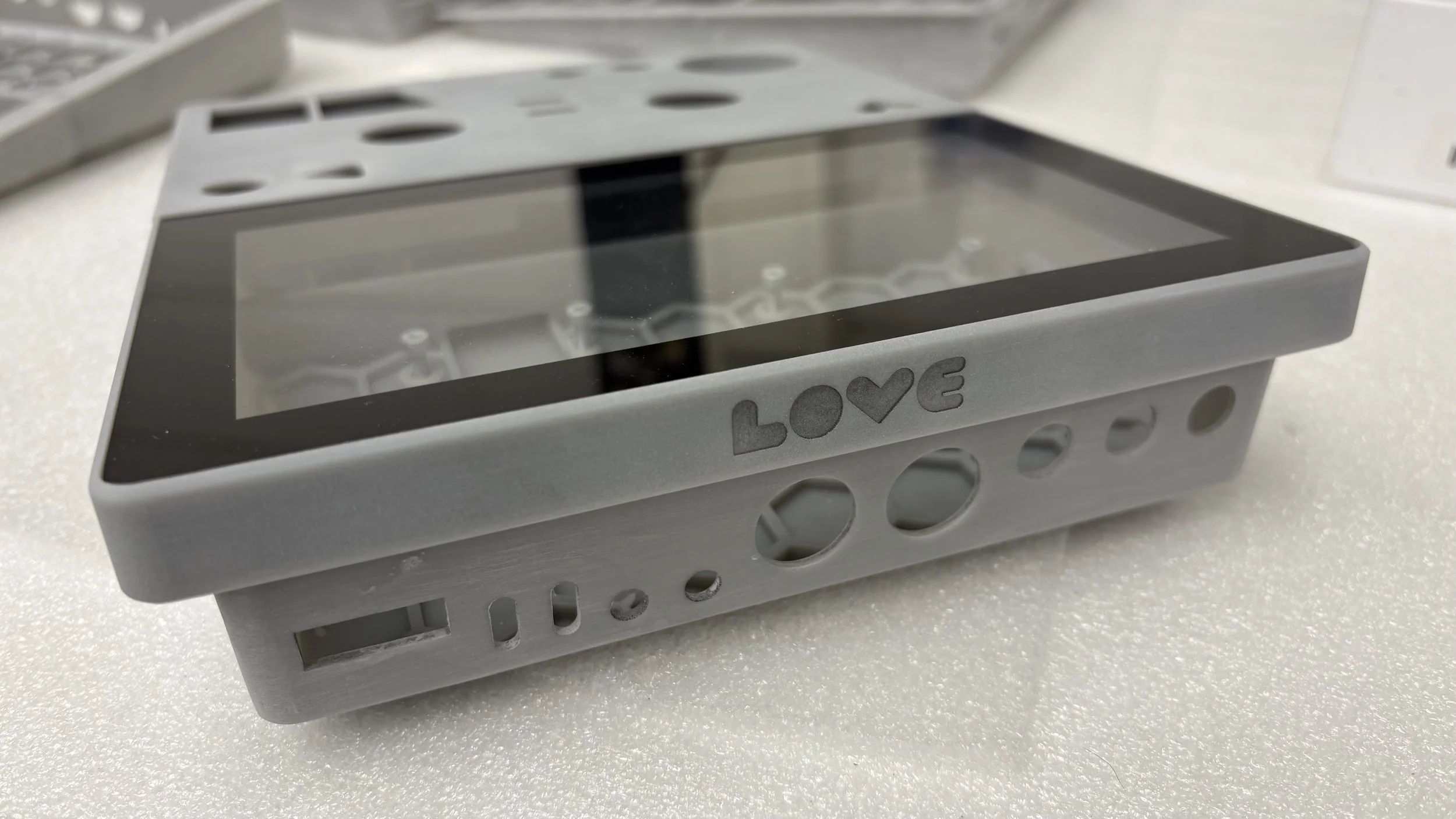 Gray electronic device with a clear screen, featuring the word 'LOVE' with a heart symbol on the side, and holes on the side for buttons or connections, placed on a white surface.