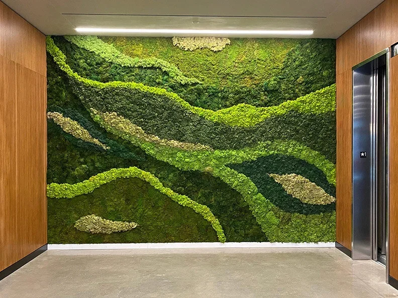 Green and tan moss wall art in a modern elevator lobby with wood-paneled walls and an elevator door.