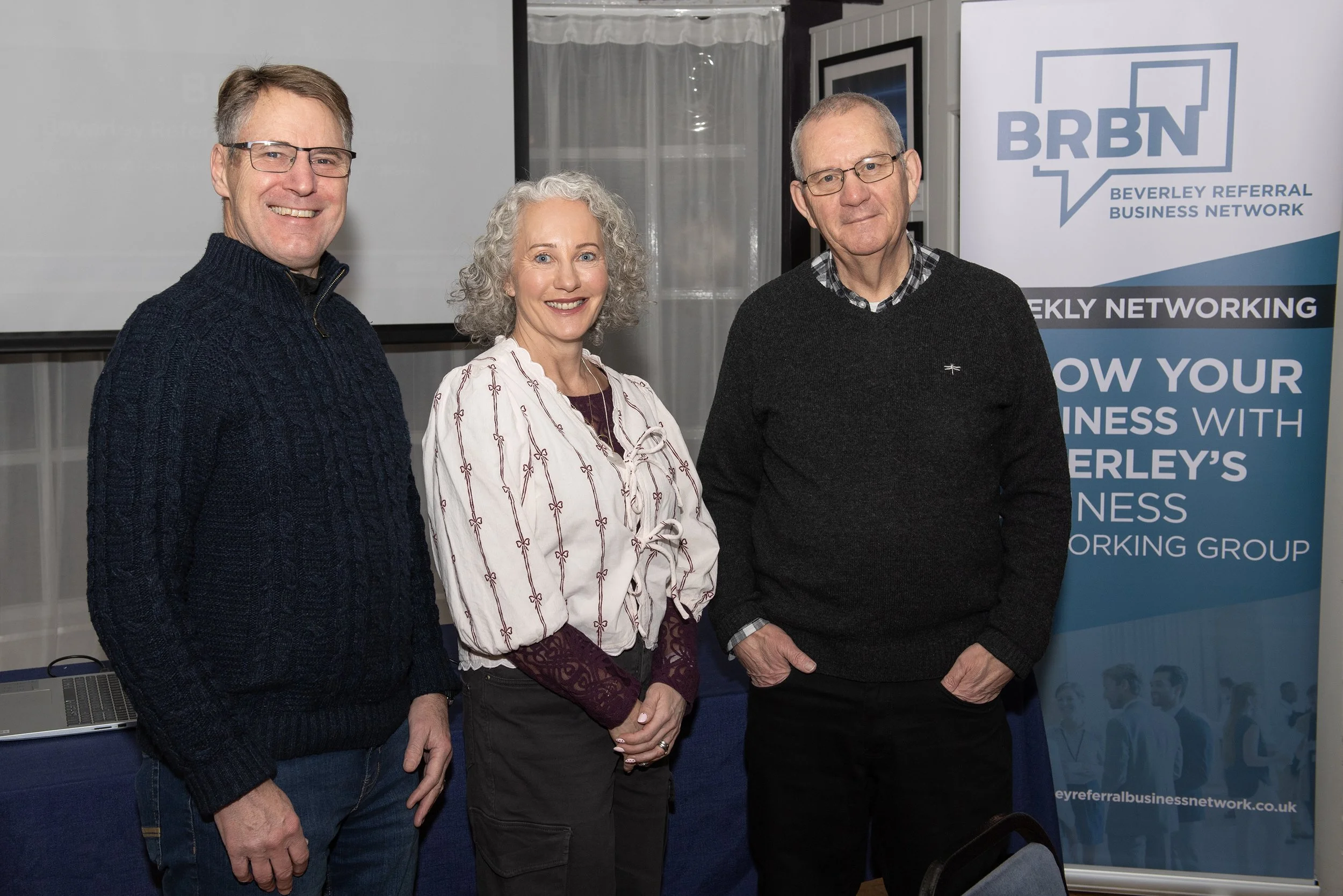 Three people standing together at a networking event, smiling, with a banner in the background that reads 'BRBN Beverley Referral Business Network'.