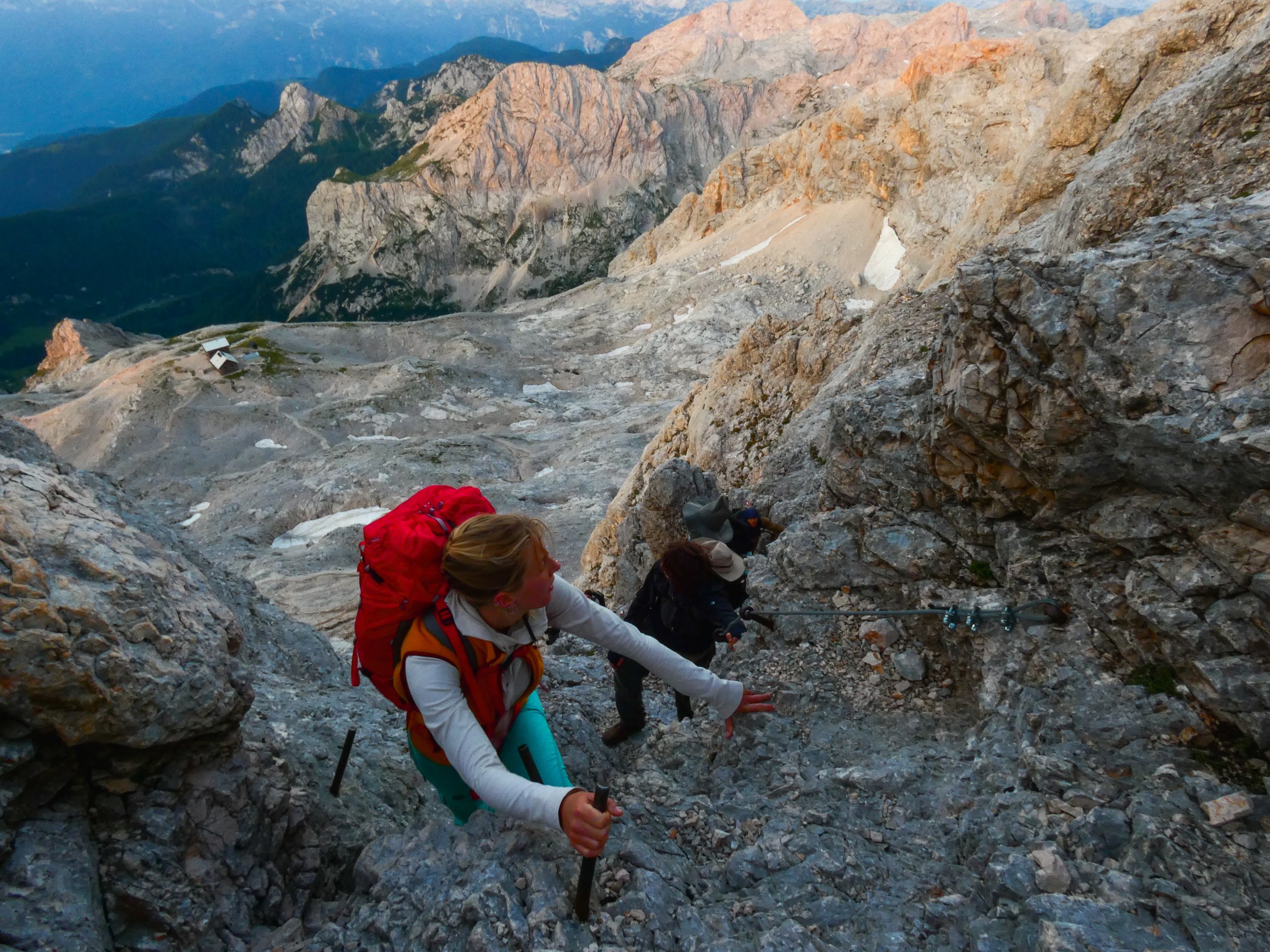 Group of climbers ascending a steep rocky mountain slope, with rugged mountain peaks in the background during sunrise.