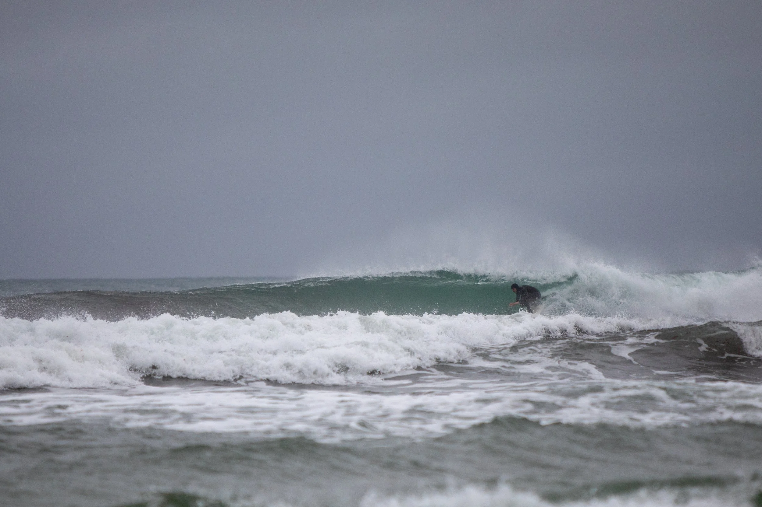 A person surfing on a wave in the ocean during overcast weather.