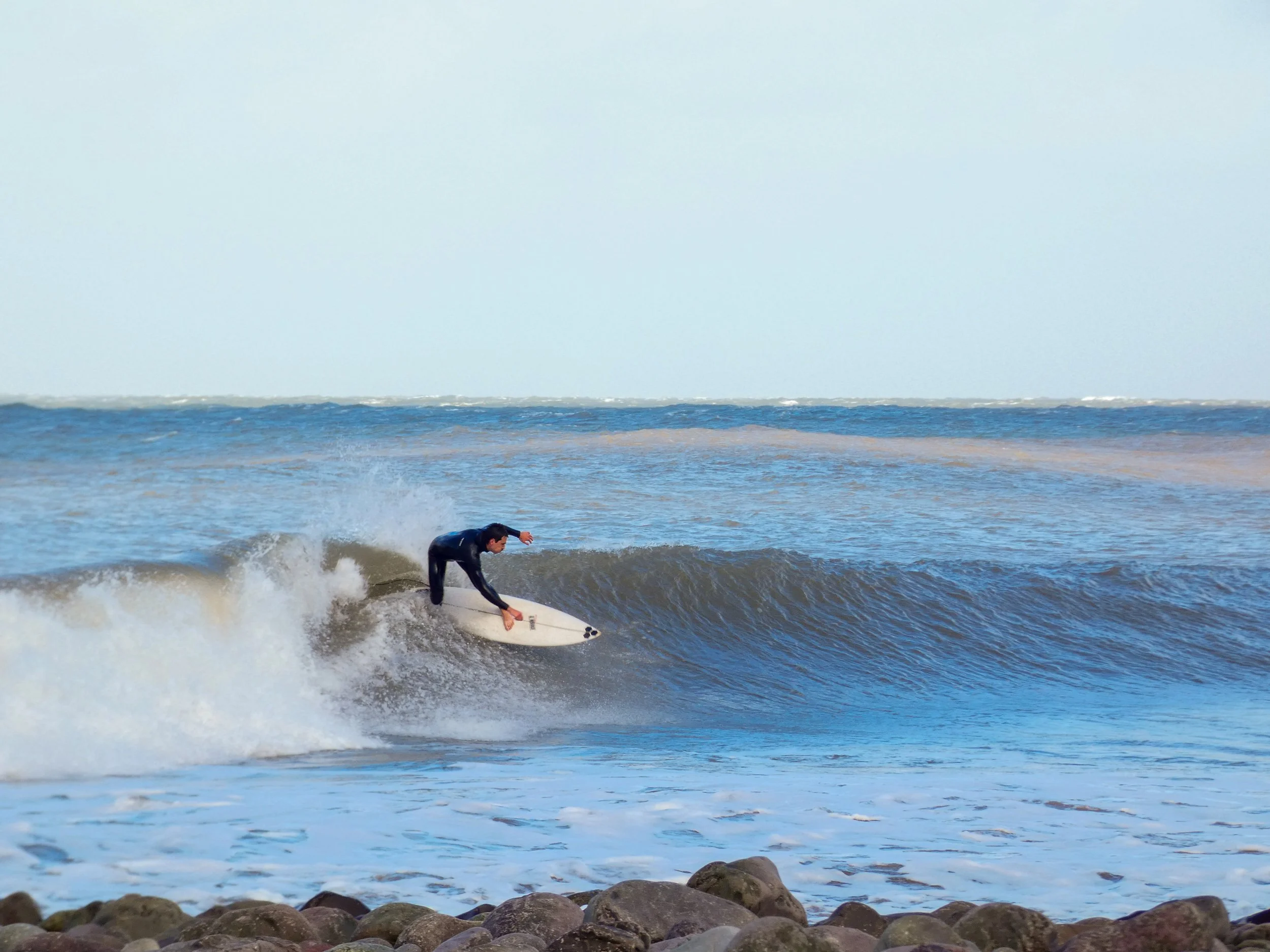 Person surfing on a wave near a rocky shoreline in the ocean.