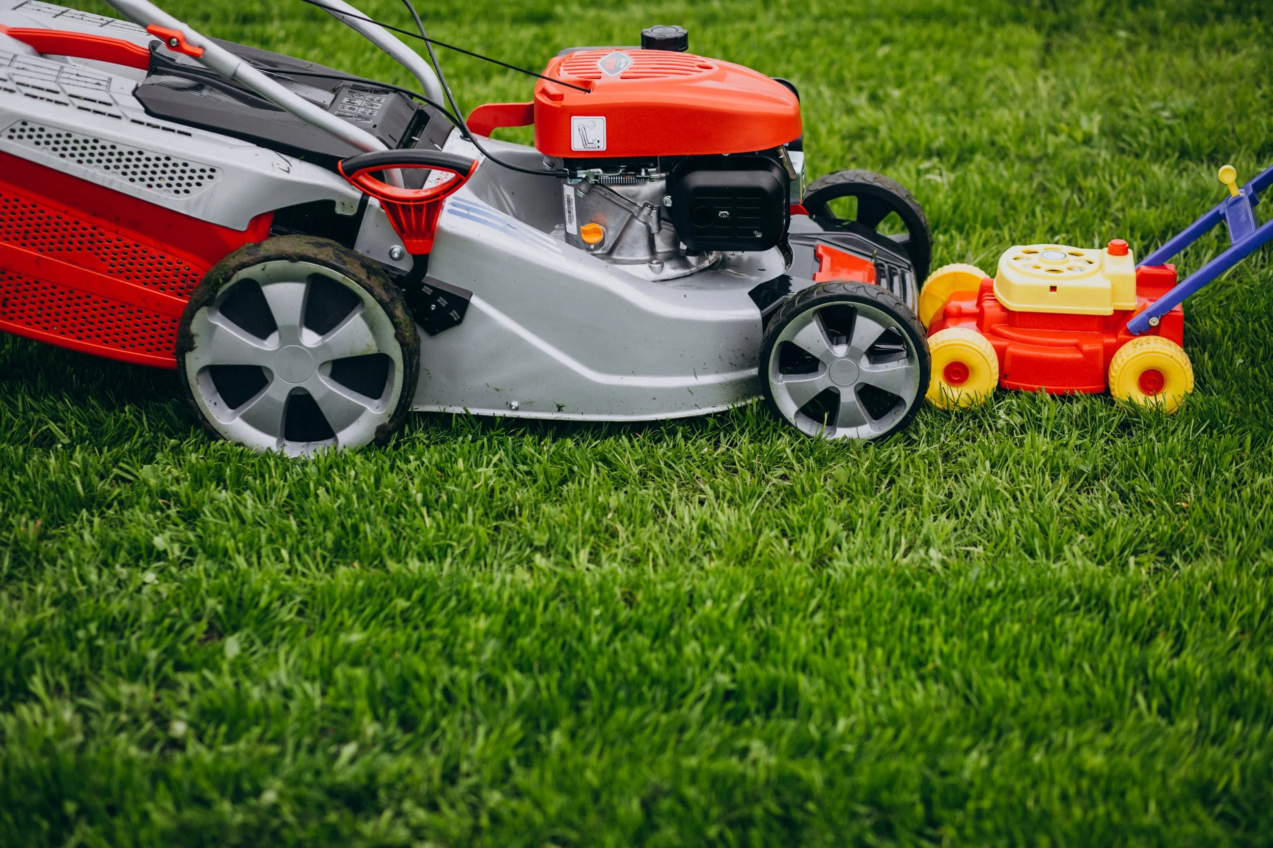 A lawnmower and a small toy ride-on lawnmower placed on a grassy lawn.