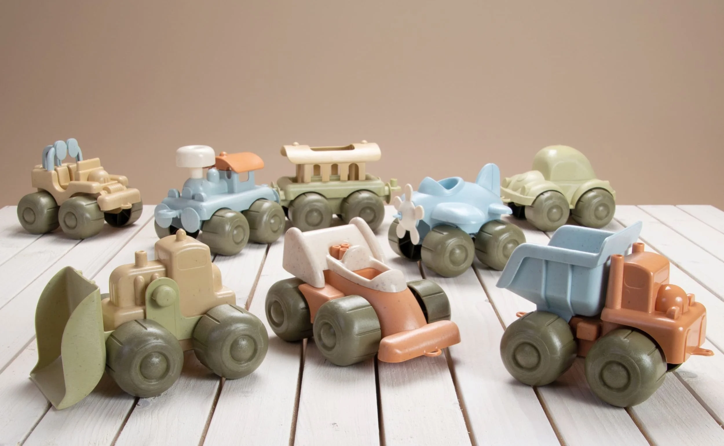 Collection of vintage-style toy construction vehicles, including bulldozers, dump trucks, and loaders, arranged on a white wooden surface.