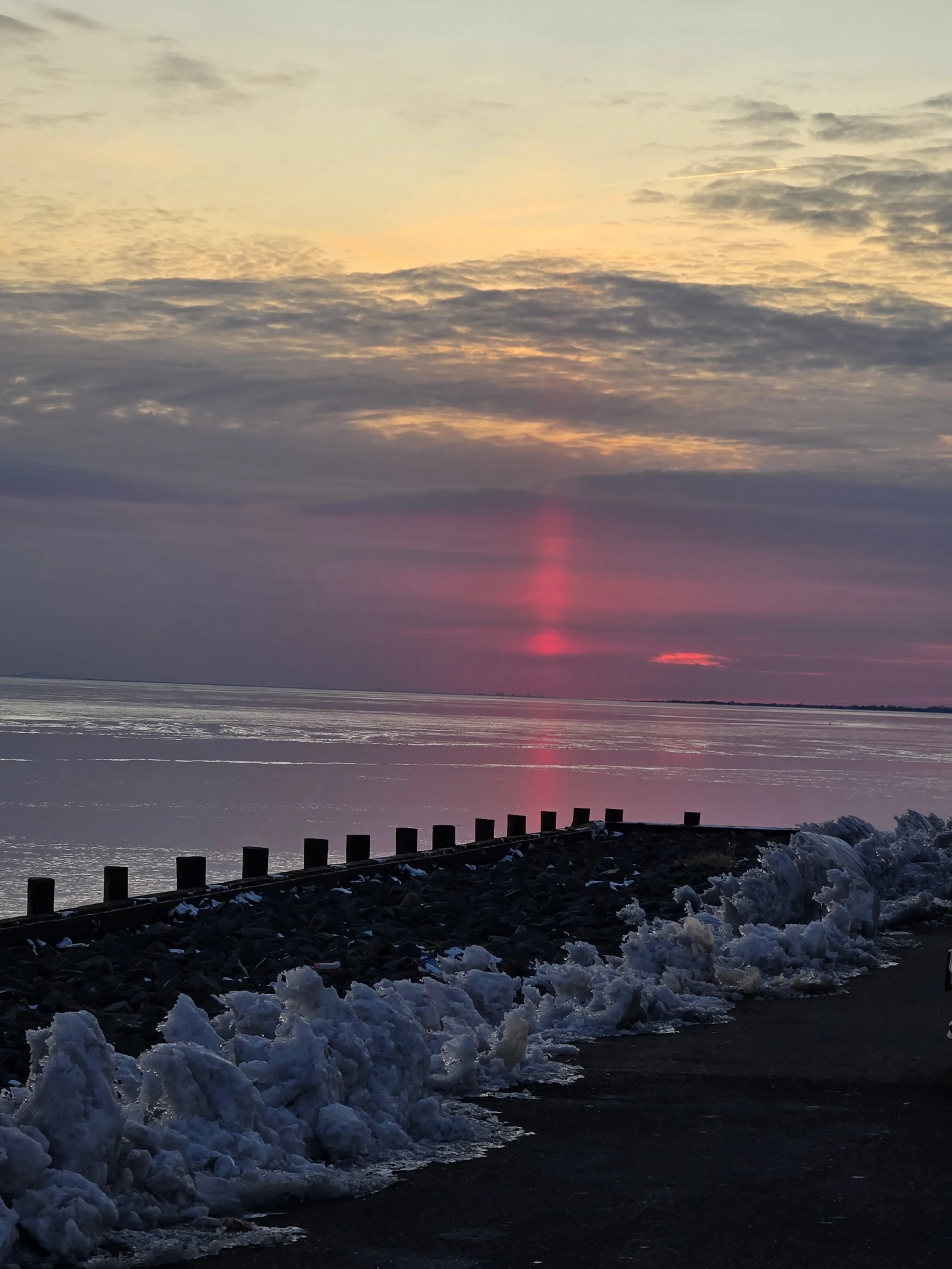 Frozen Great South Bay with solid ice formations and a jetty extending into the still water under a muted winter sky.