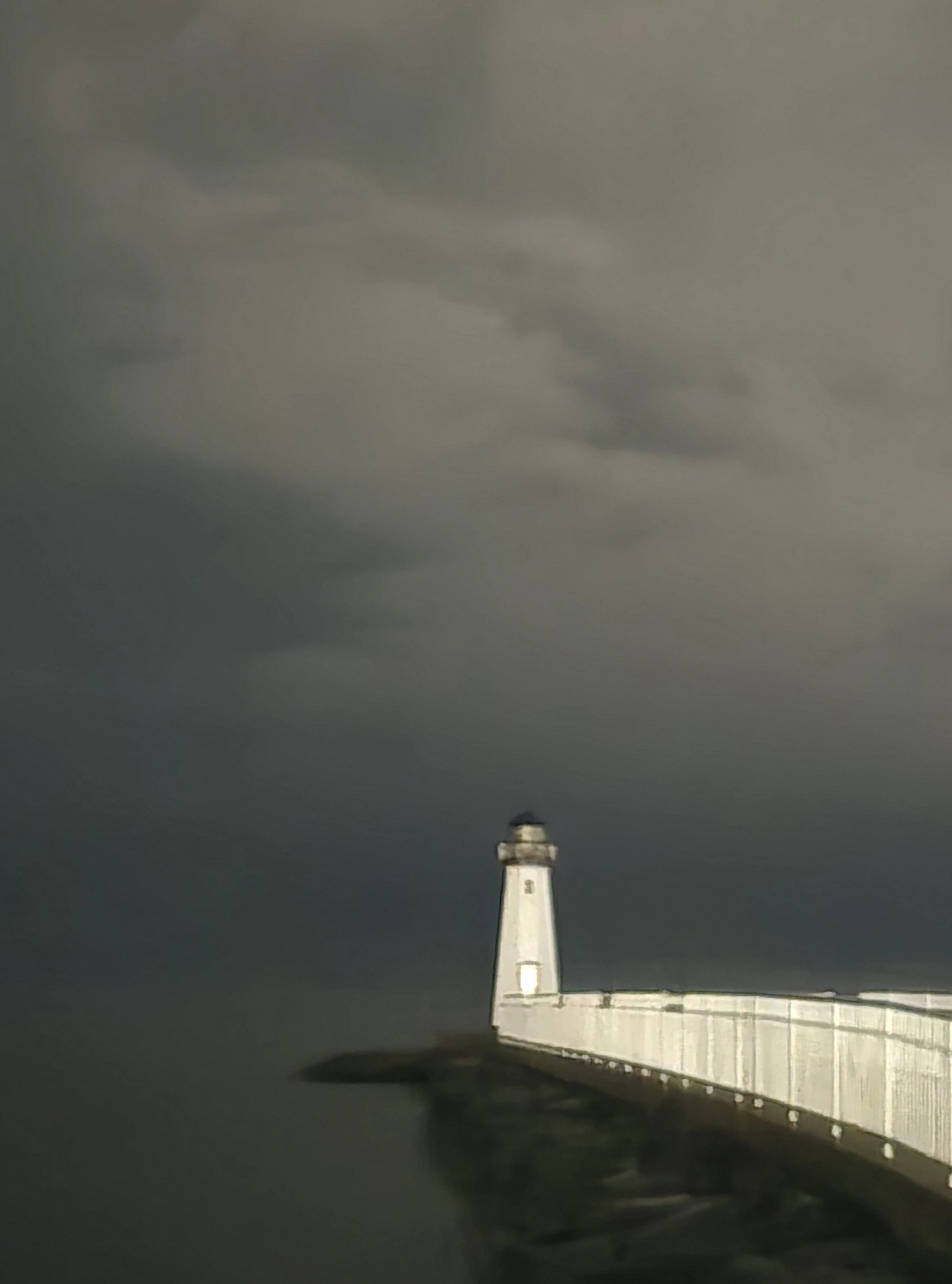 Lighthouse at the end of a long pier under heavy fog, structure fading into dark water