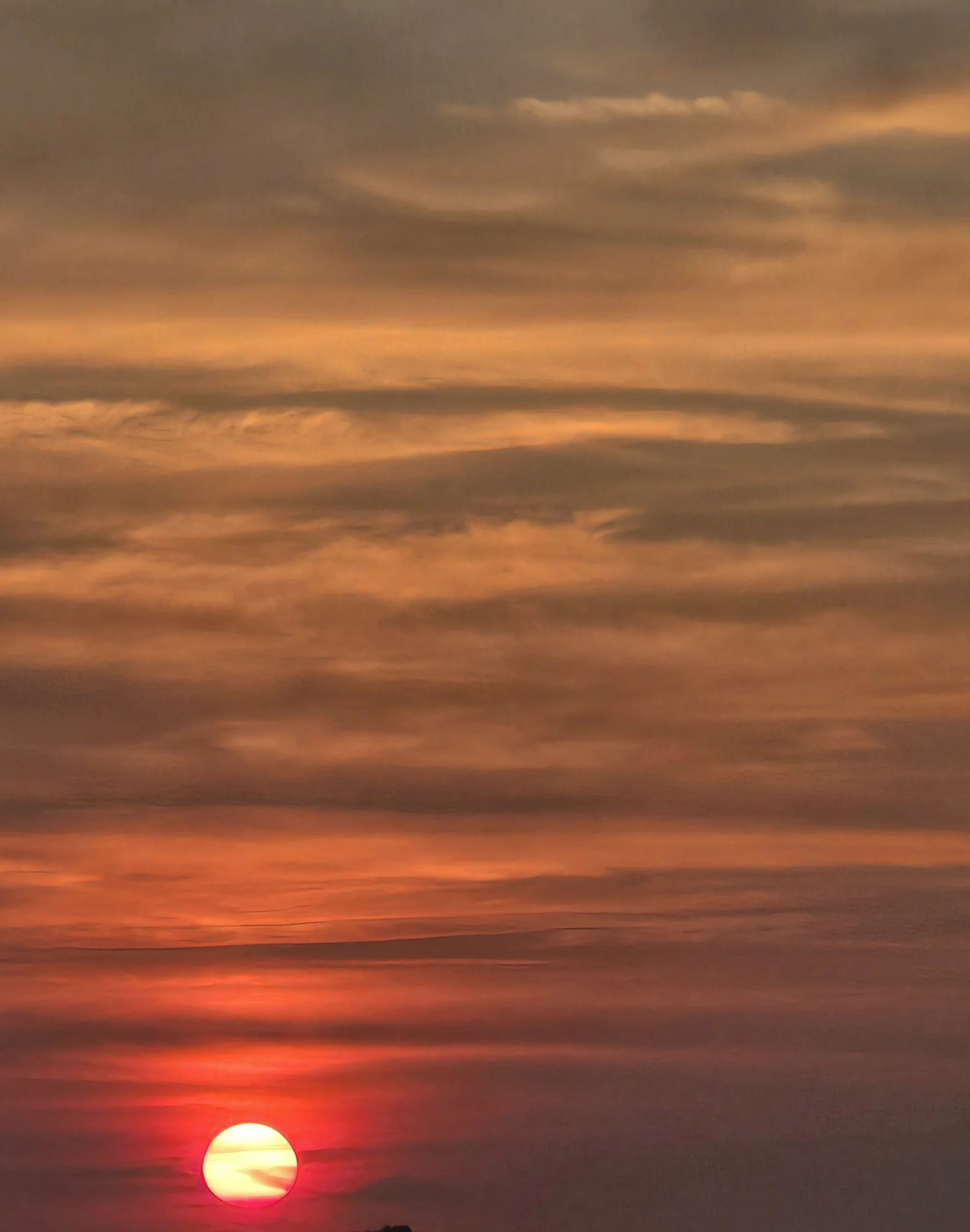 Deep red sun low in a hazy sky with layered clouds, glowing horizon at dusk