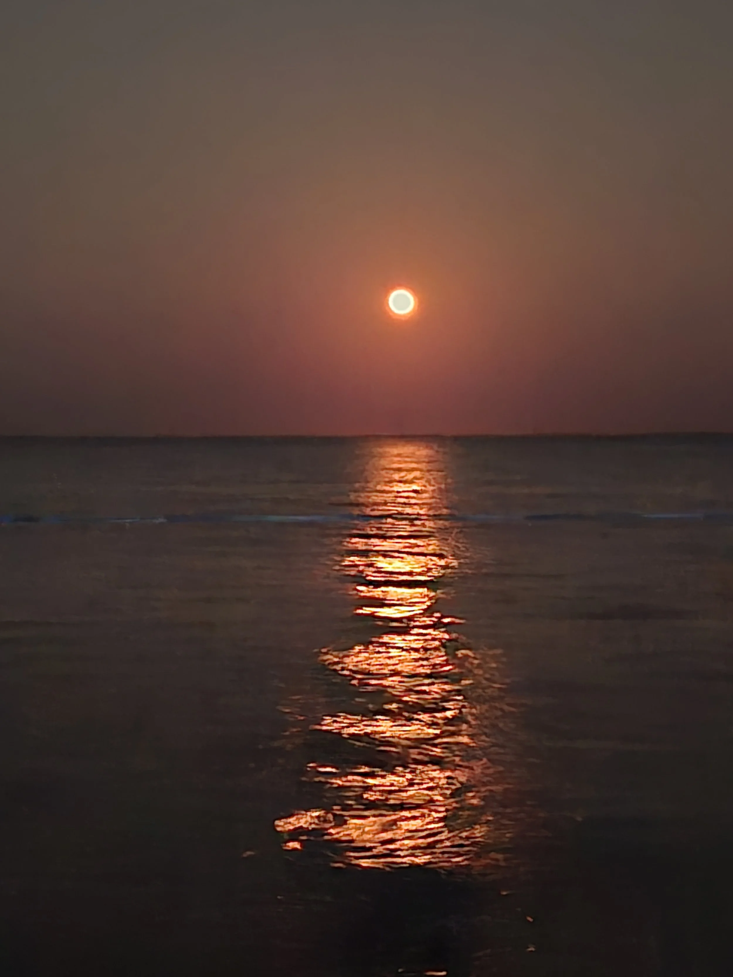 Strawberry moon rising over open water, deep red orange glow woth reflection stretching across the surface