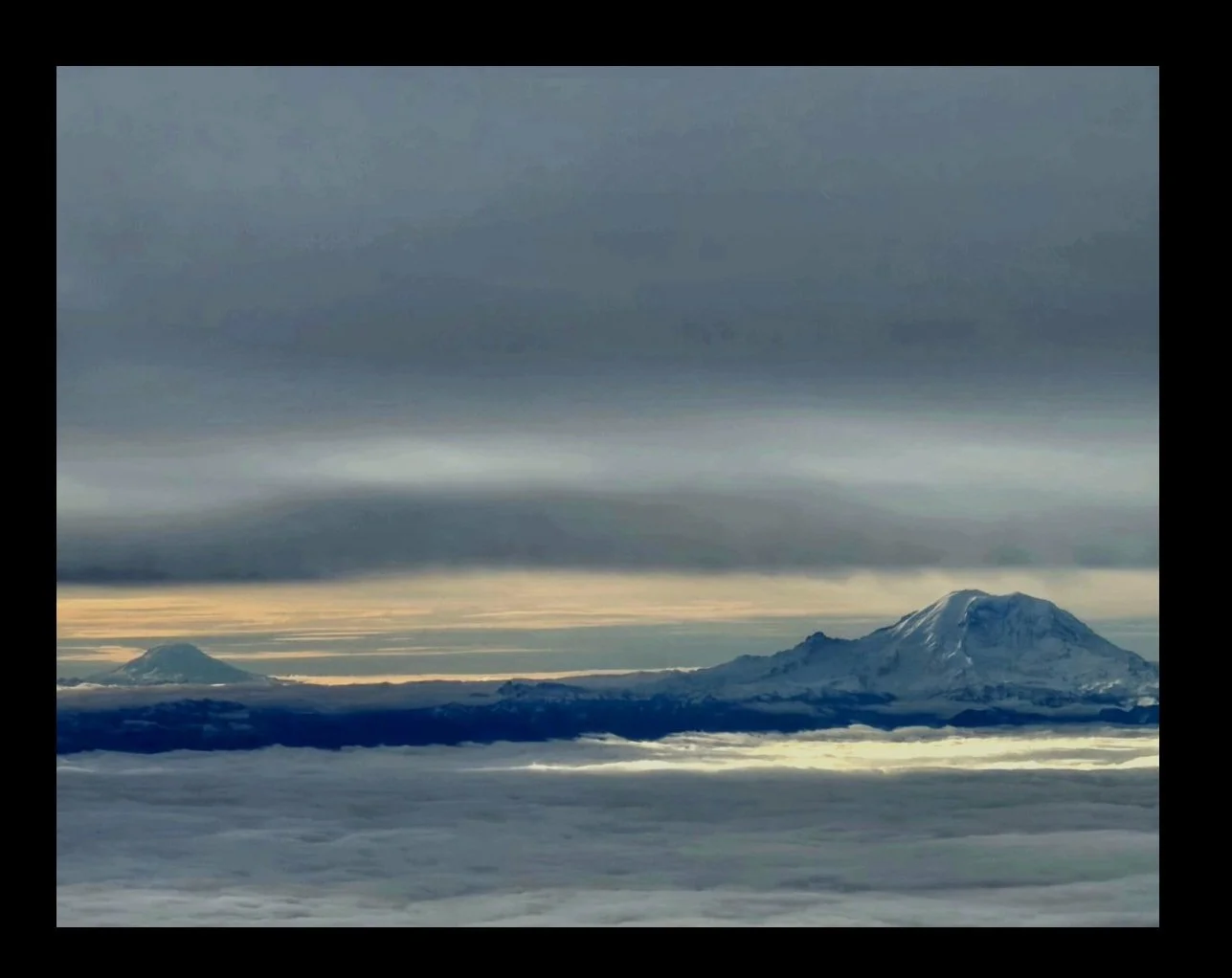 Aerial view above a cloud layer with Mount Rainier in Washington rising through the clouds beneath soft sky light
