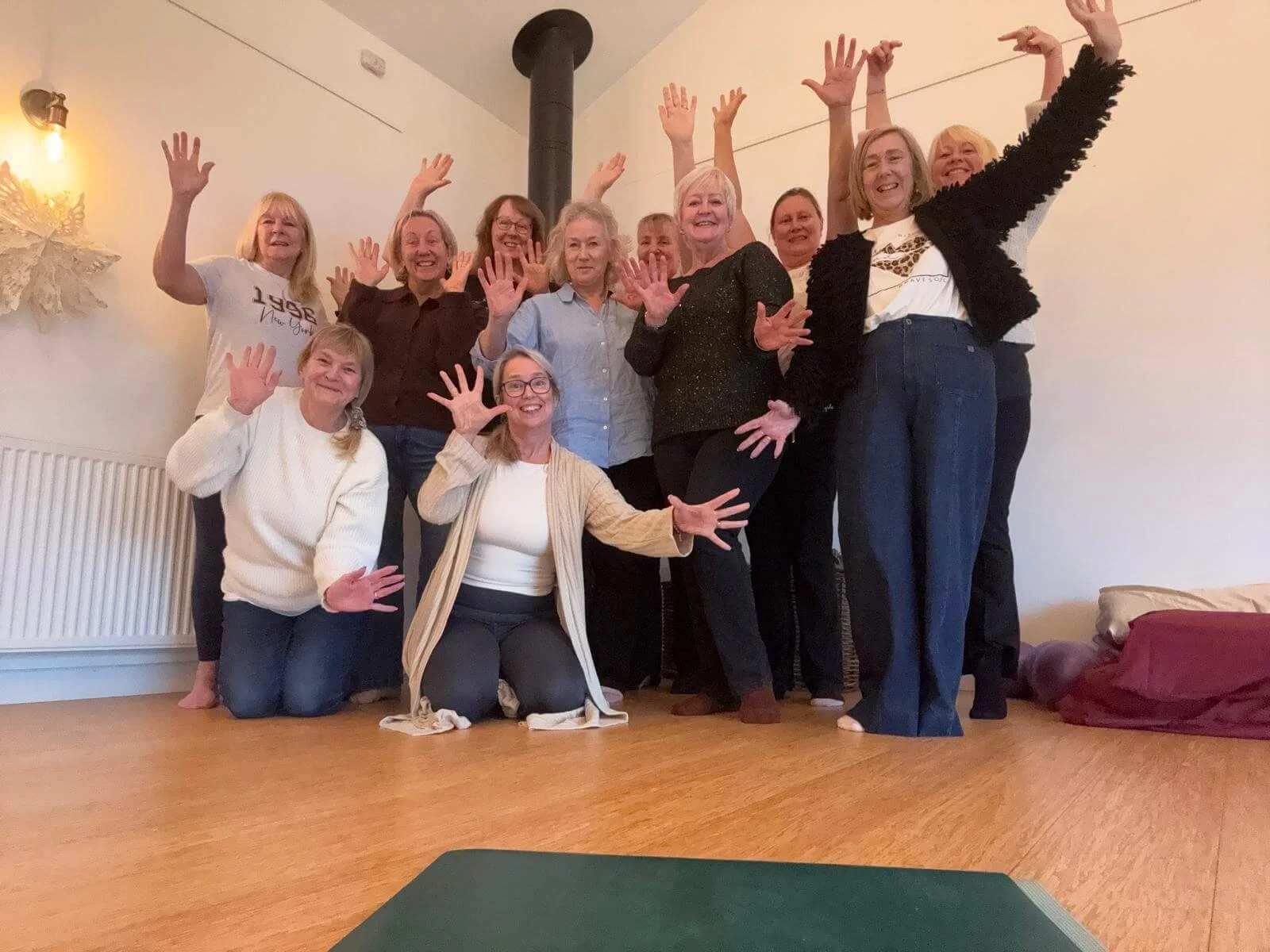 Group of smiling women gathered indoors, posing with raised hands during a celebration or gathering.
