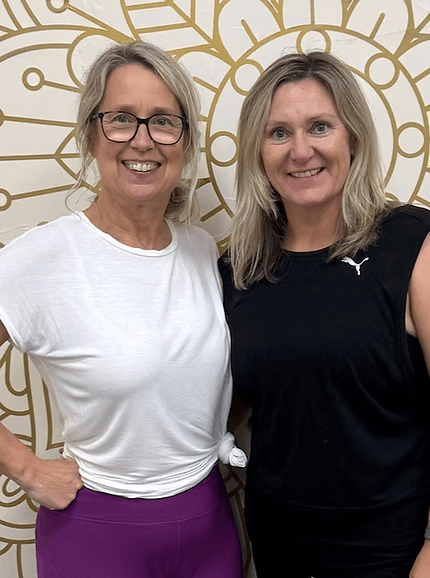 Two women standing together in front of a gold geometric wall design, smiling at the camera.
