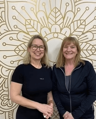 Two women smiling in front of a decorative wall with floral patterns.