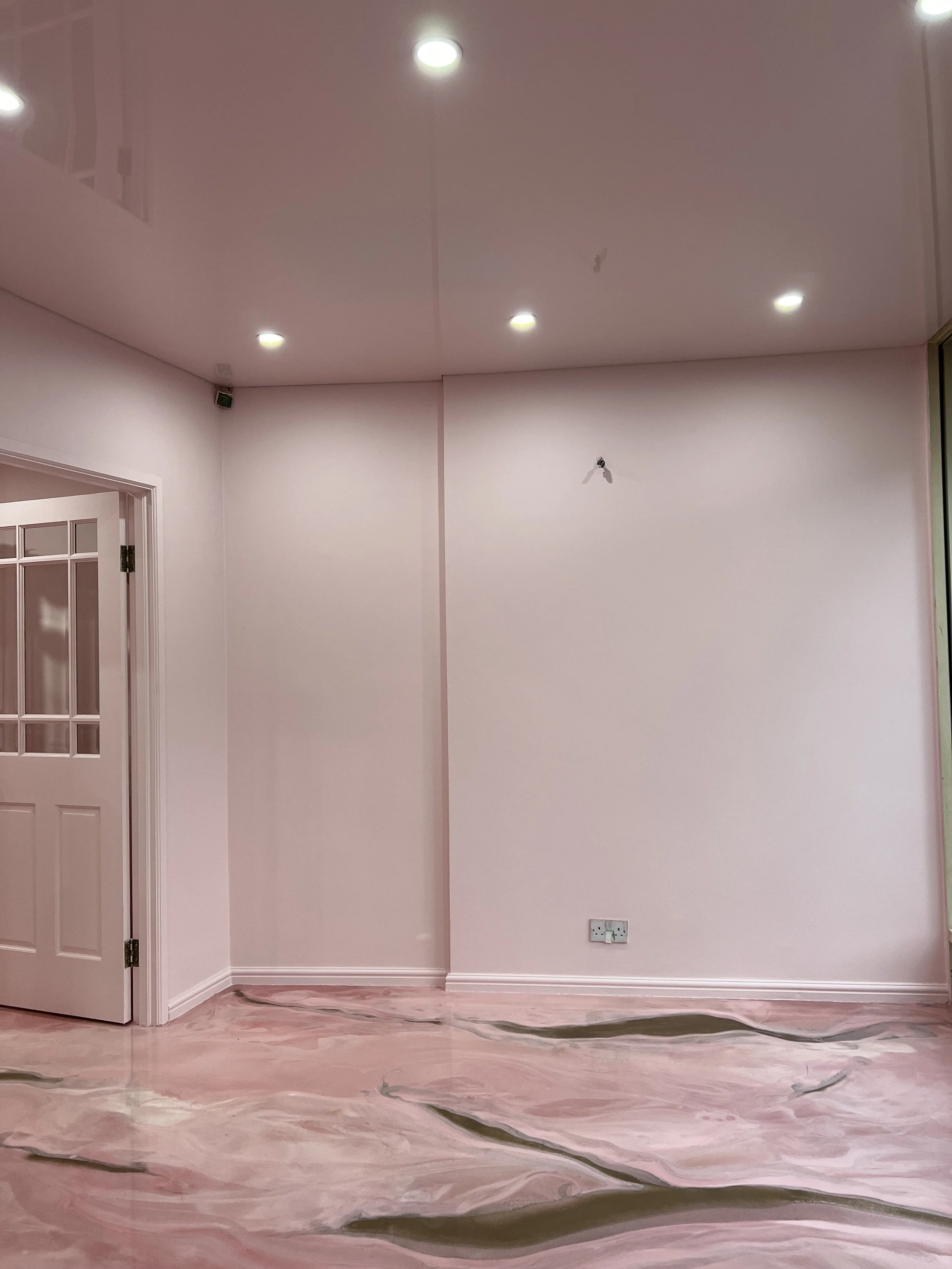 Empty room with pink walls, marble floor, ceiling lights, and a door with glass panels.