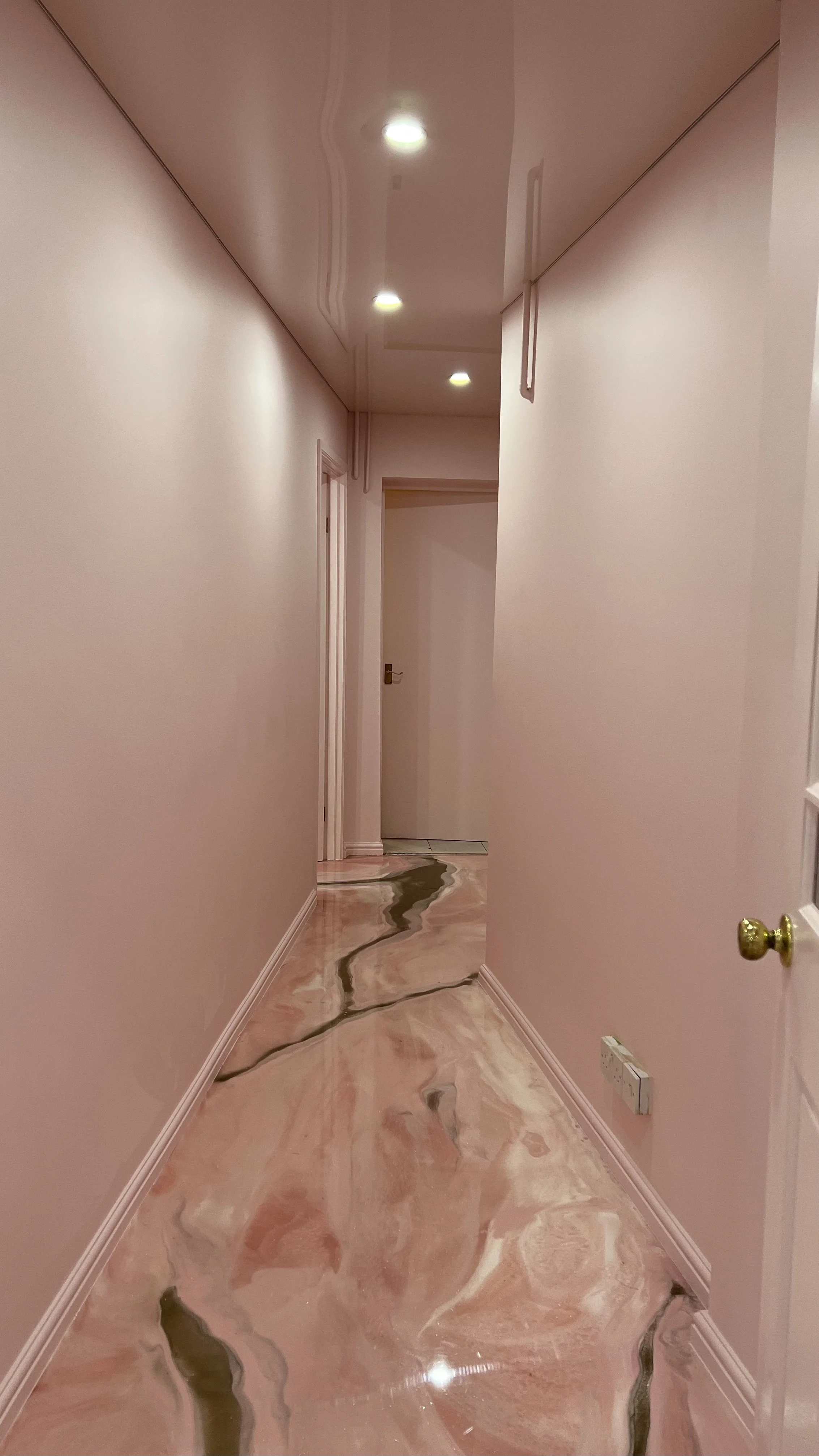 Empty hallway with pinkish marble flooring and white walls, illuminated by ceiling lights.