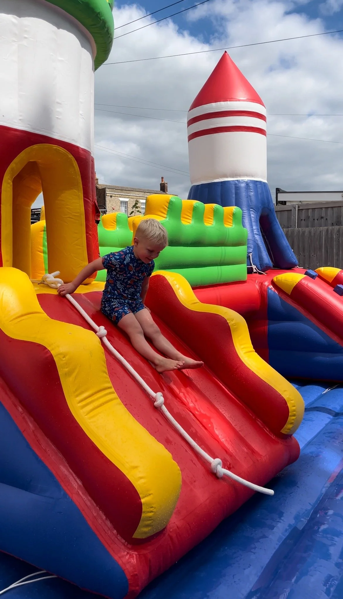 A young boy enjoying the Splash Park at Curve Water Sports, a colourful inflatable bouncy castle and slide on a partly cloudy day.