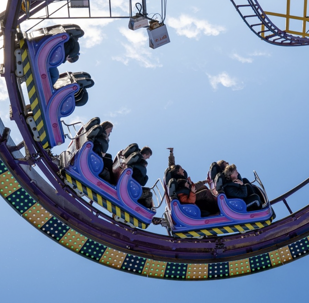People riding a colorful roller coaster at Clacton Pier against a blue sky with some clouds.