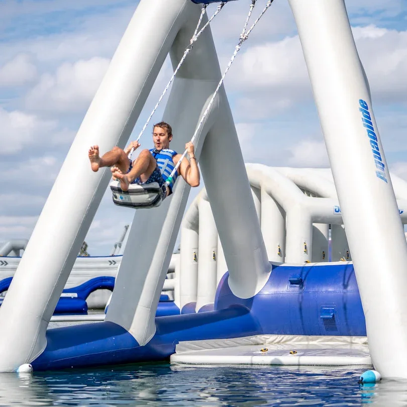 The 'Catapult' showing a person on a large inflatable water swing at a water park, swinging over the water with a partly cloudy sky in the background.
