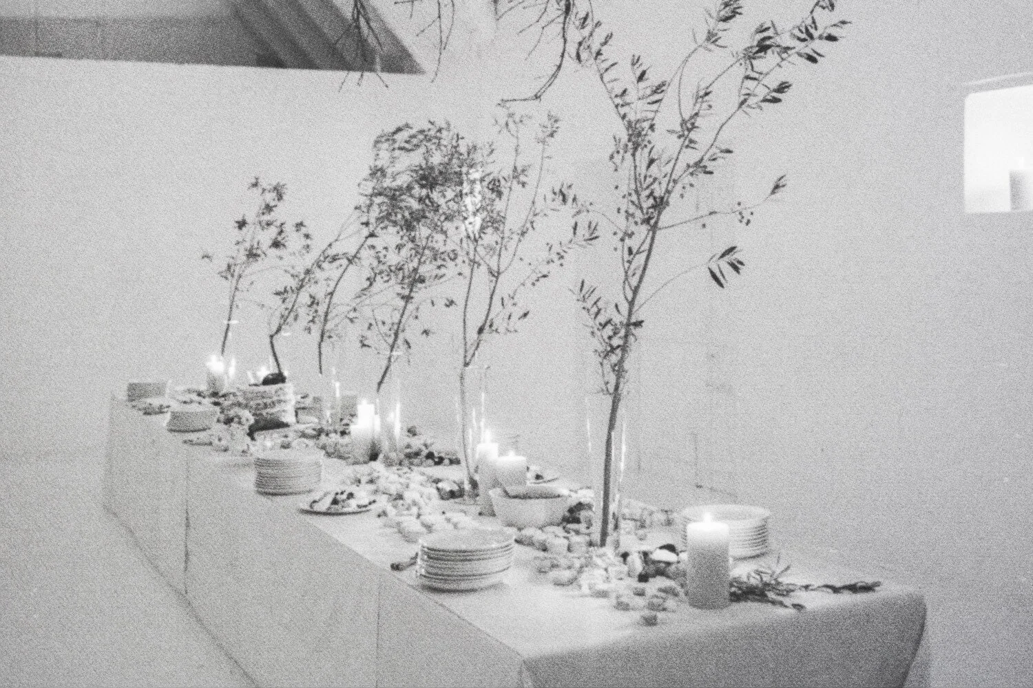 Table décorée avec des bougies allumées, des assiettes blanches, des branches d'arbre ou de bambou, et des petits cailloux ou décorations, dans une ambiance élégante et minimaliste.