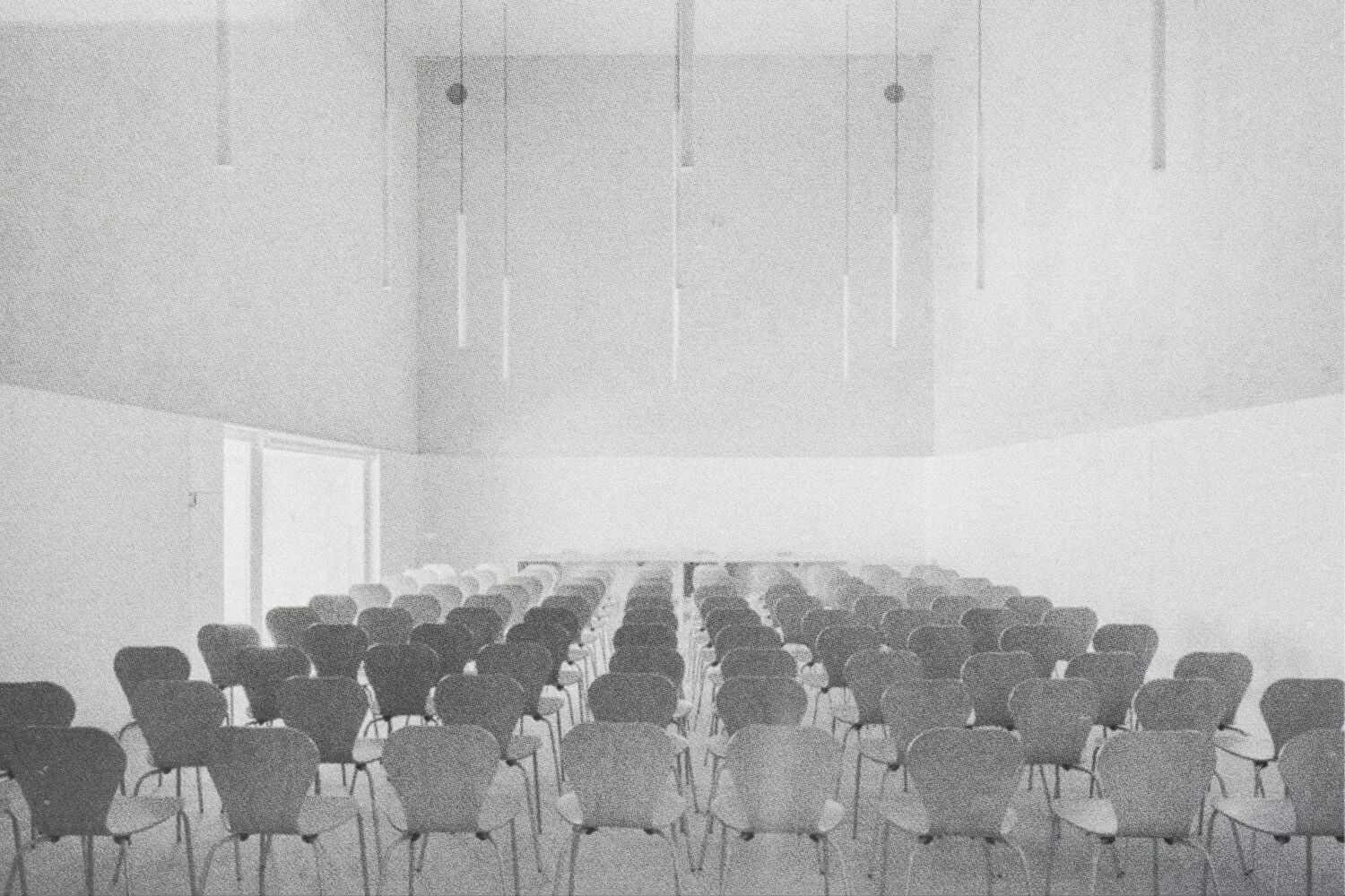 Salle de conférence vide avec de nombreuses chaises disposées en rangées et un plafond avec des pendentifs suspendus.