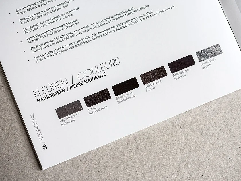 A color swatch chart titled "KLEUREN / COULEURS" showing five shades of black and gray, with labels in Dutch, German, and French. The shades include Belgian Hardstone (dark honey), Jasberg (polished/honed), Zimbabwe Black (polished/honed), Zimbabwe B